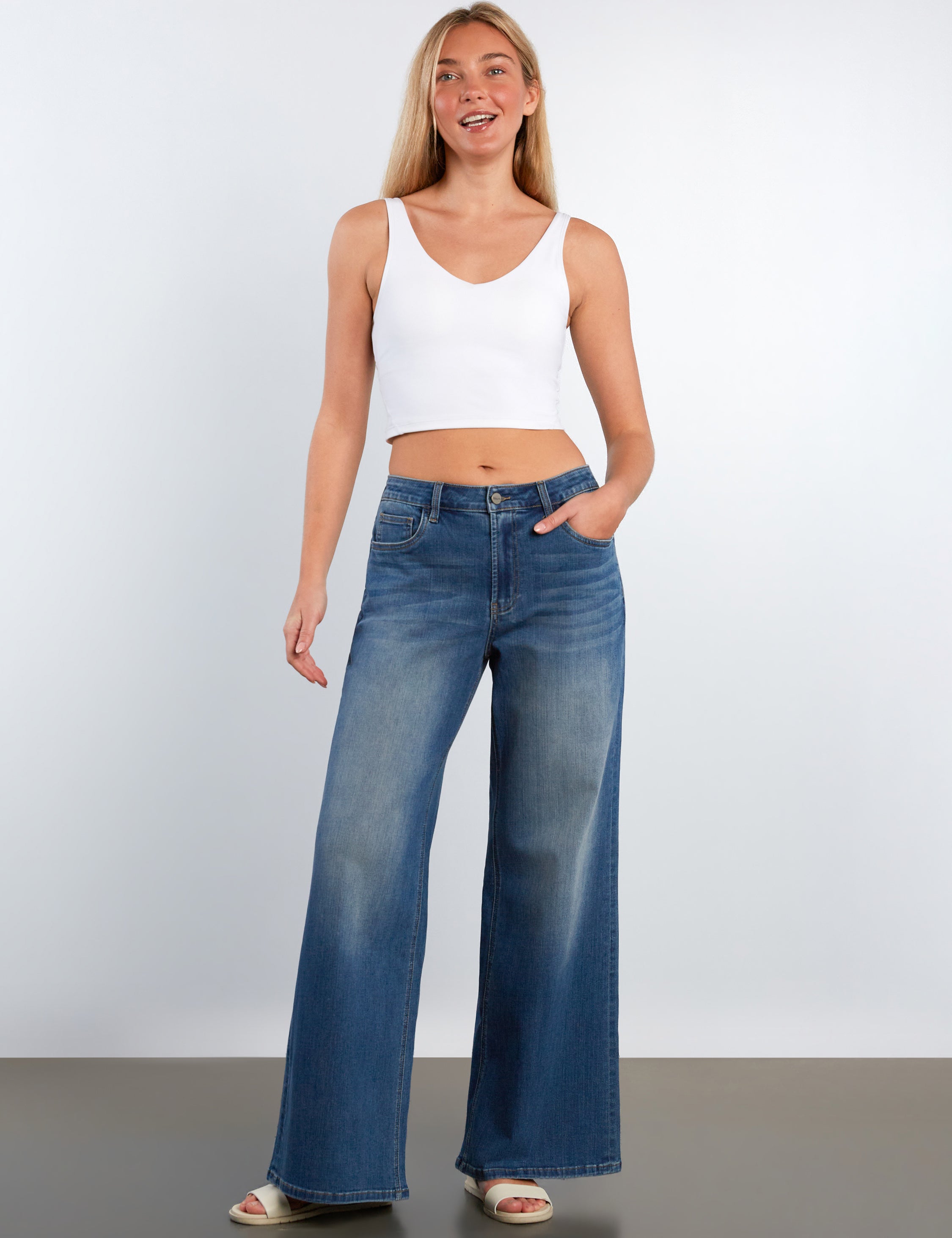 Woman wearing a white tank top and blue jeans against a plain background