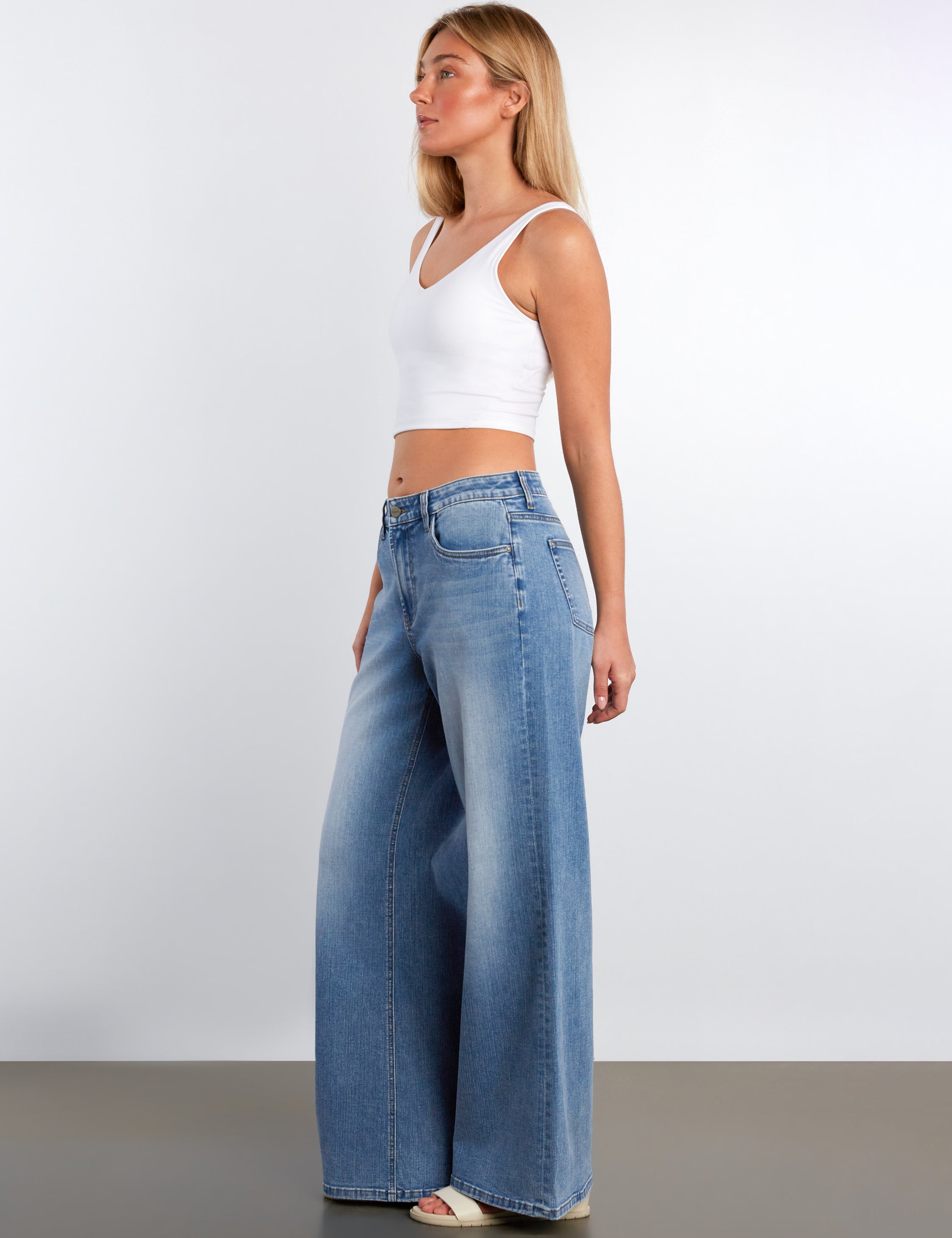 Woman wearing a white tank top and blue jeans against a plain background