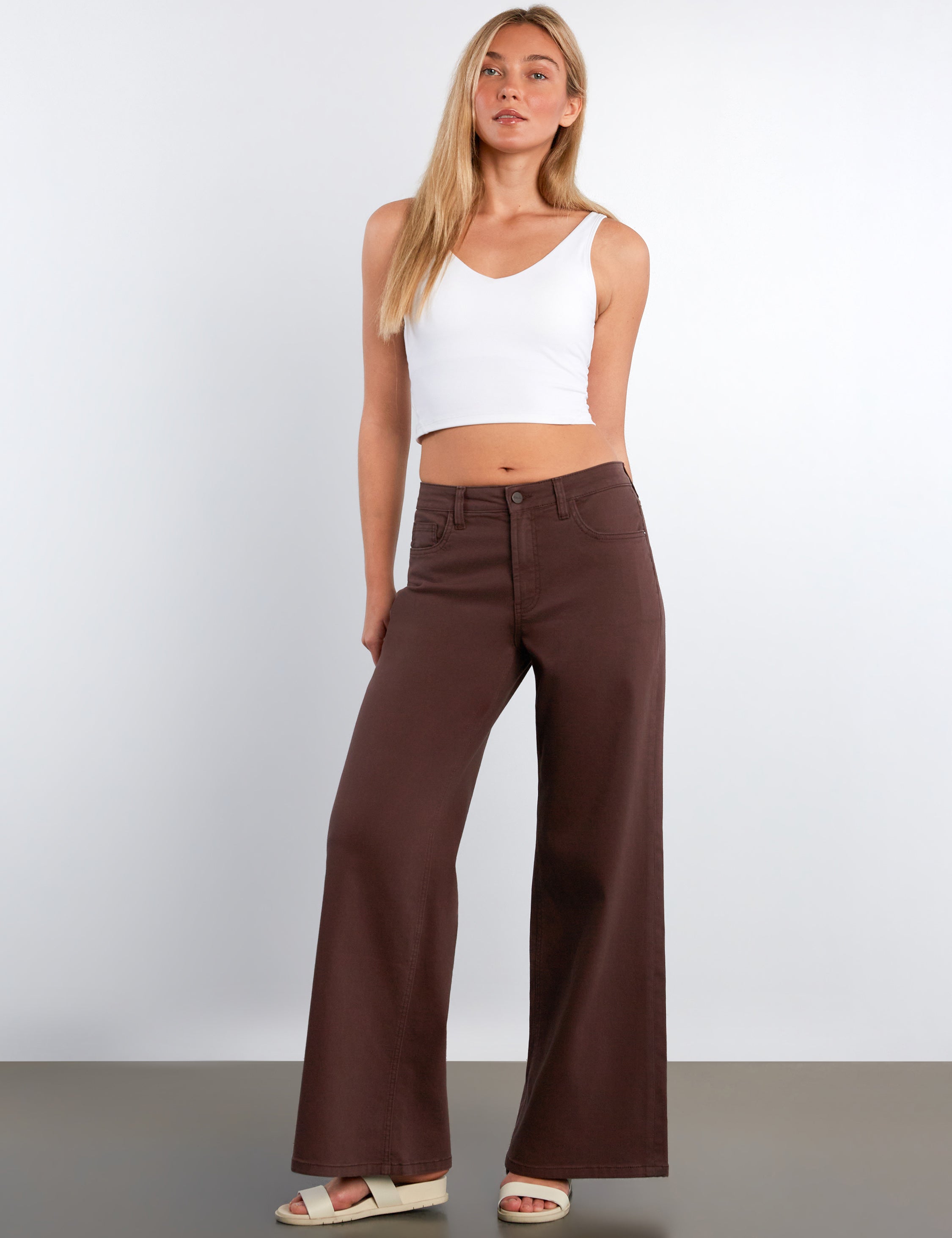 Woman wearing a white top and brown wide-leg pants against a plain background