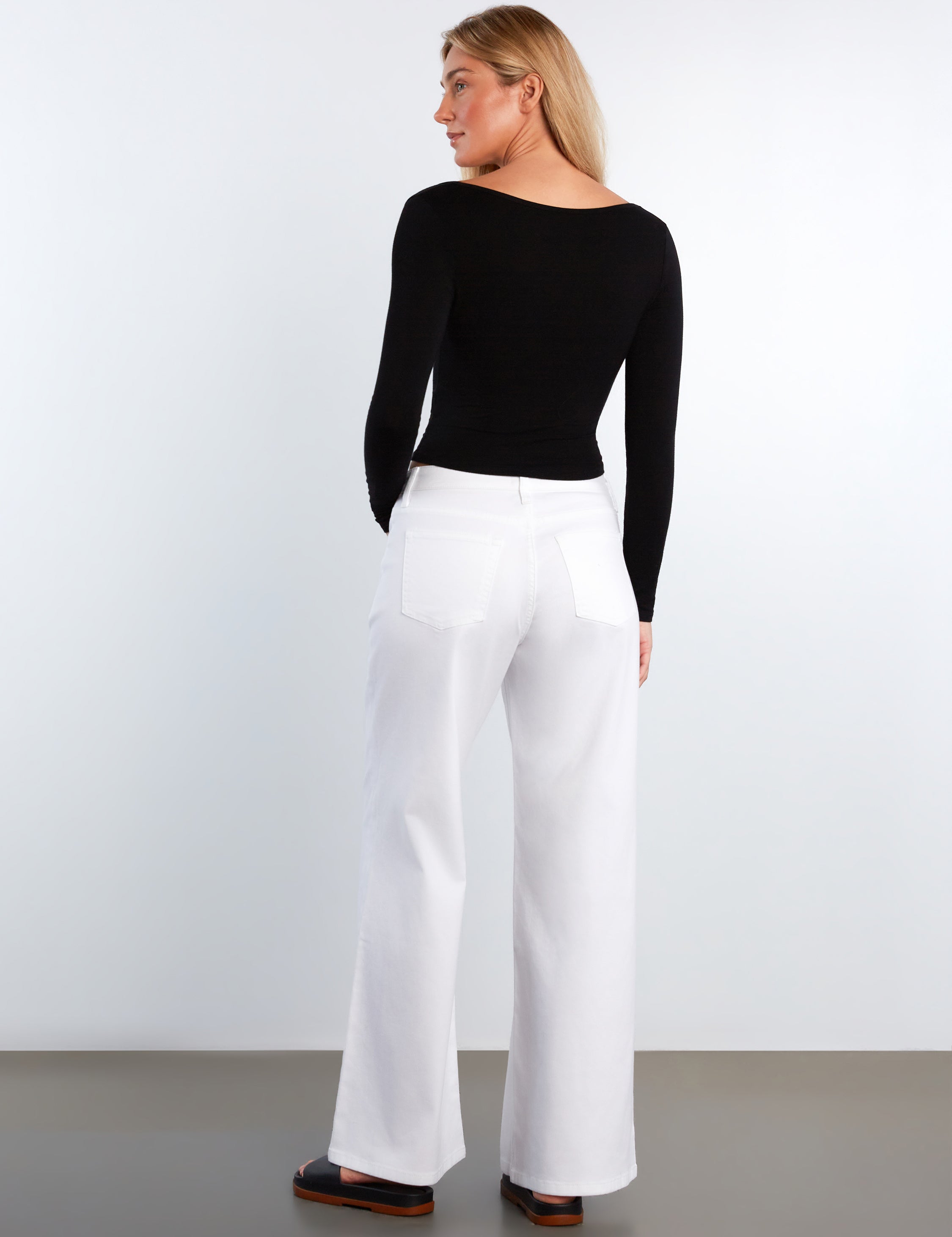 Woman wearing a black top and white pants against a plain background
