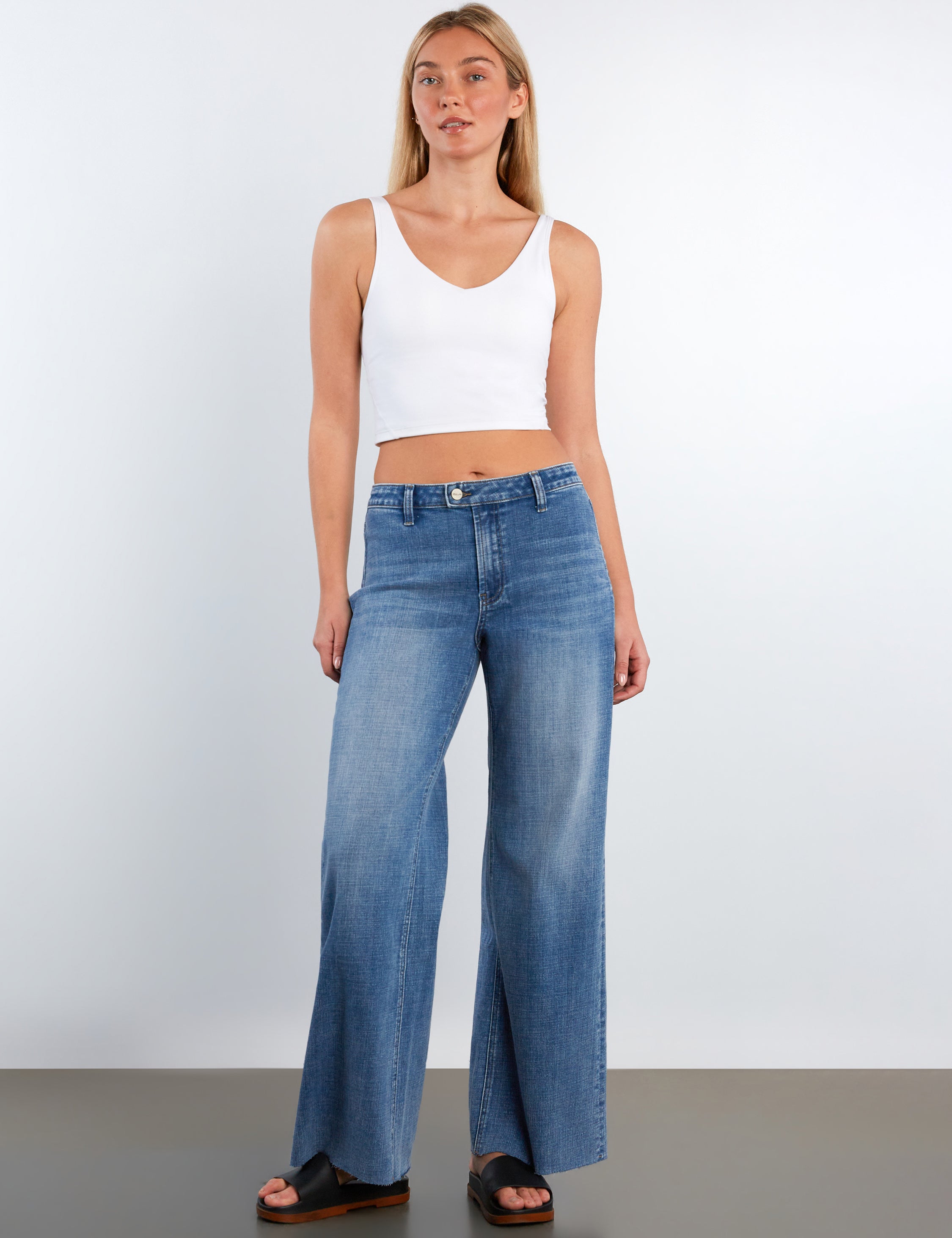 Woman wearing blue jeans and a white top on a plain background
