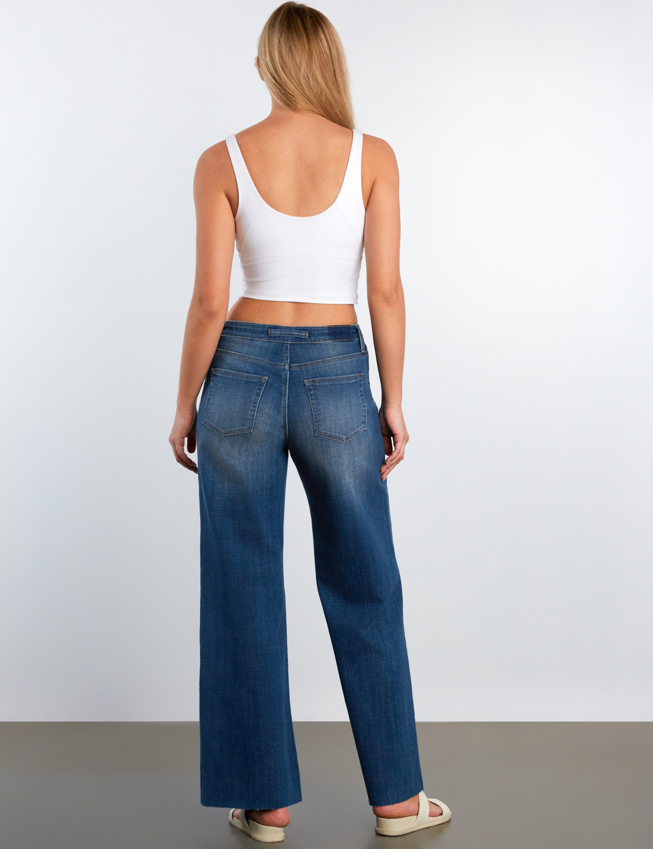 Woman wearing blue jeans and a white top against a plain background
