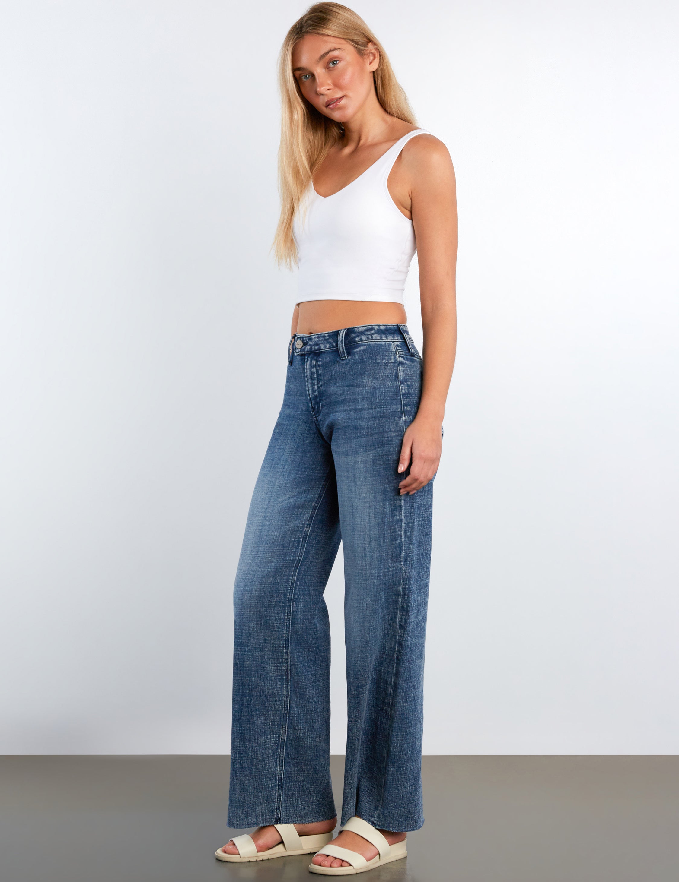 Woman wearing a white tank top and blue jeans against a plain background