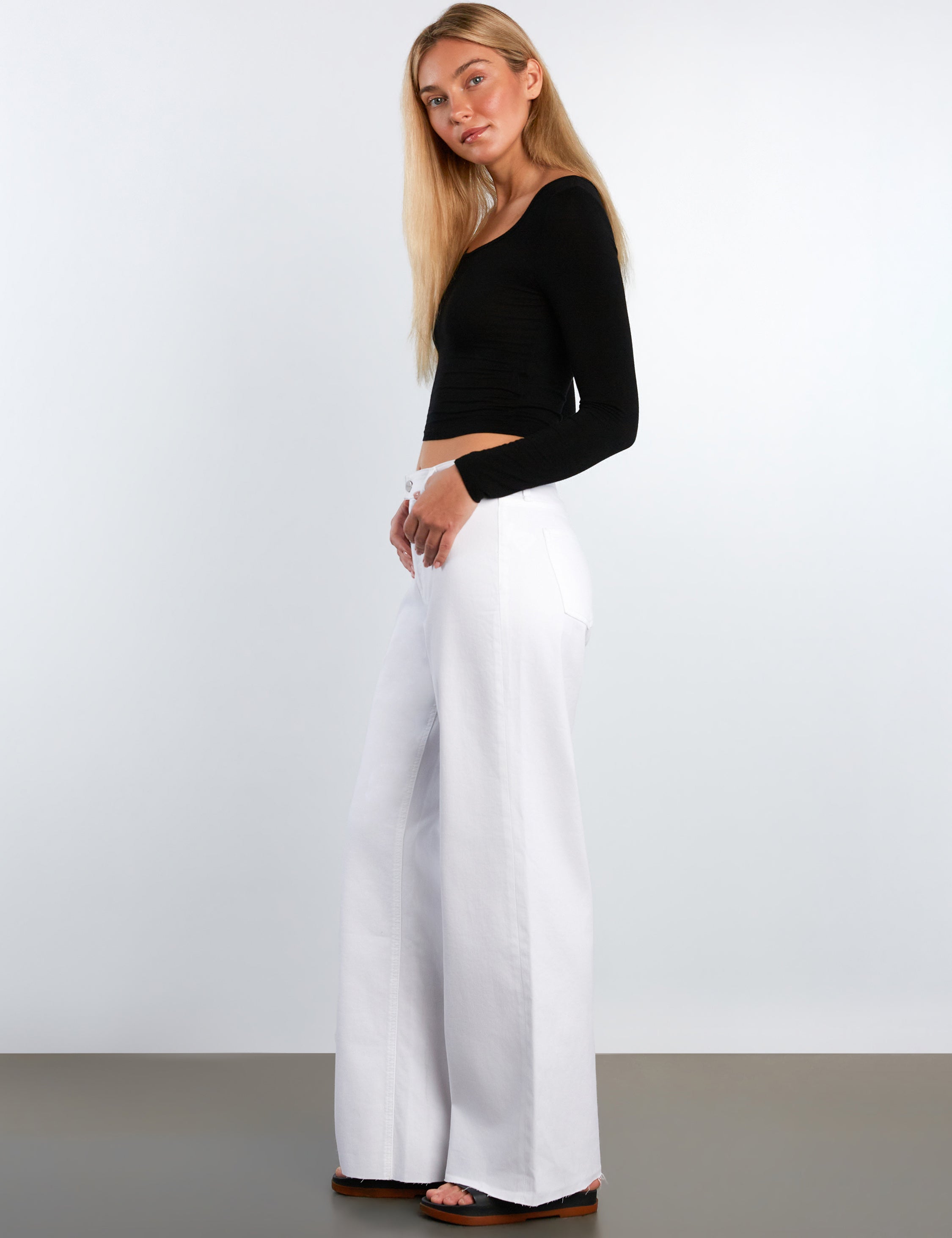 Woman wearing a black top and white pants against a plain background