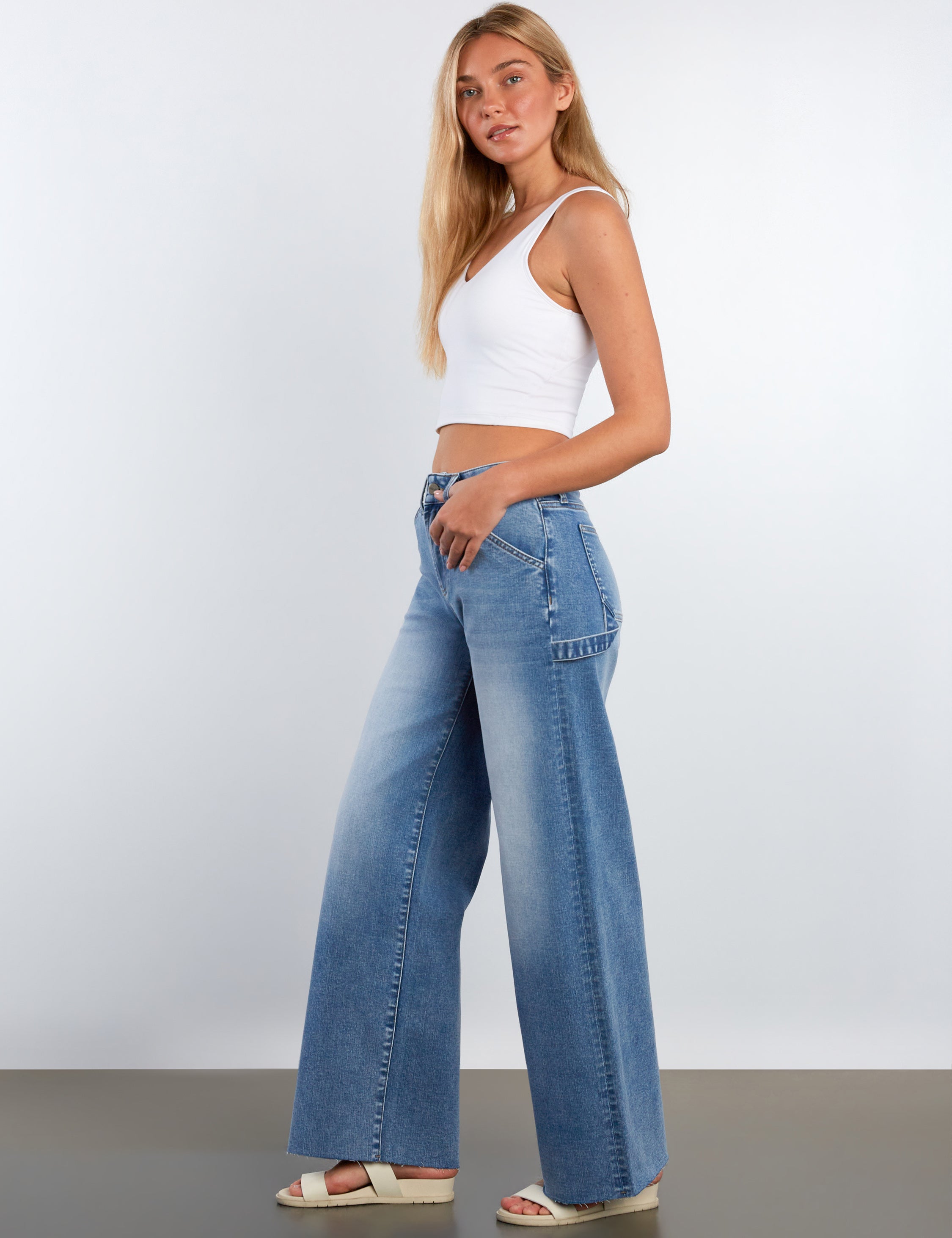 Woman wearing a white top and blue jeans against a plain background