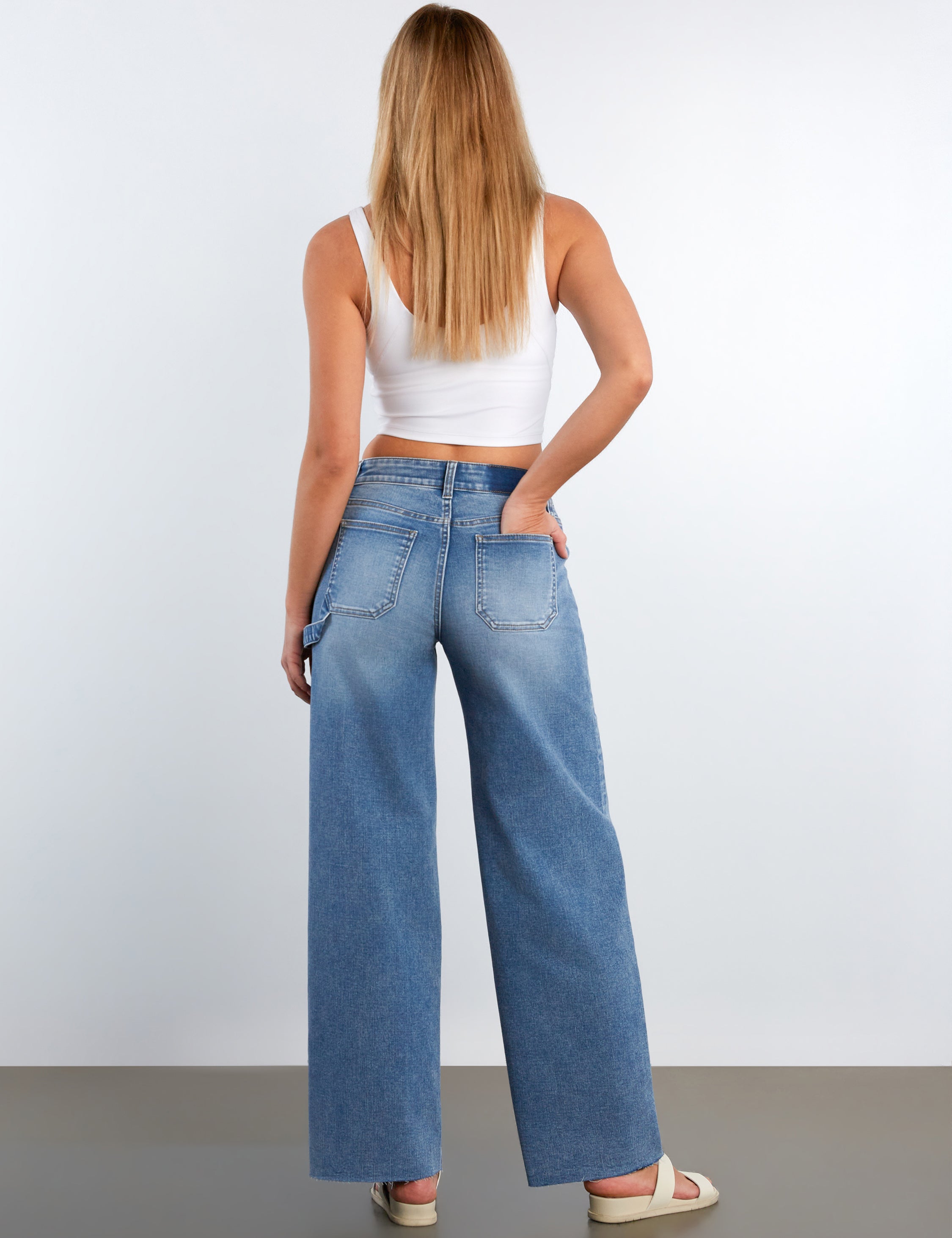 Woman wearing blue jeans and a white top against a plain background