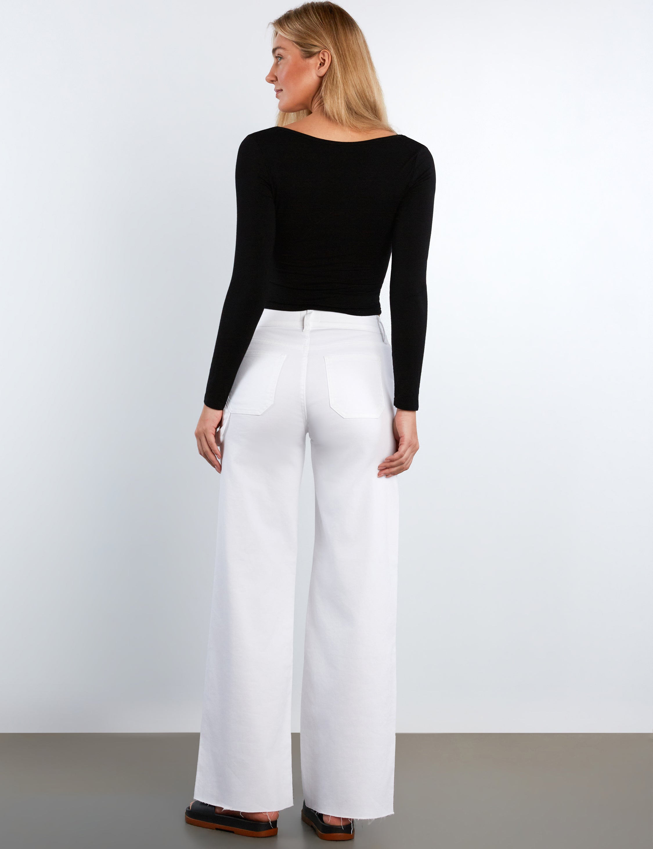 Woman wearing a black top and white pants on a plain background