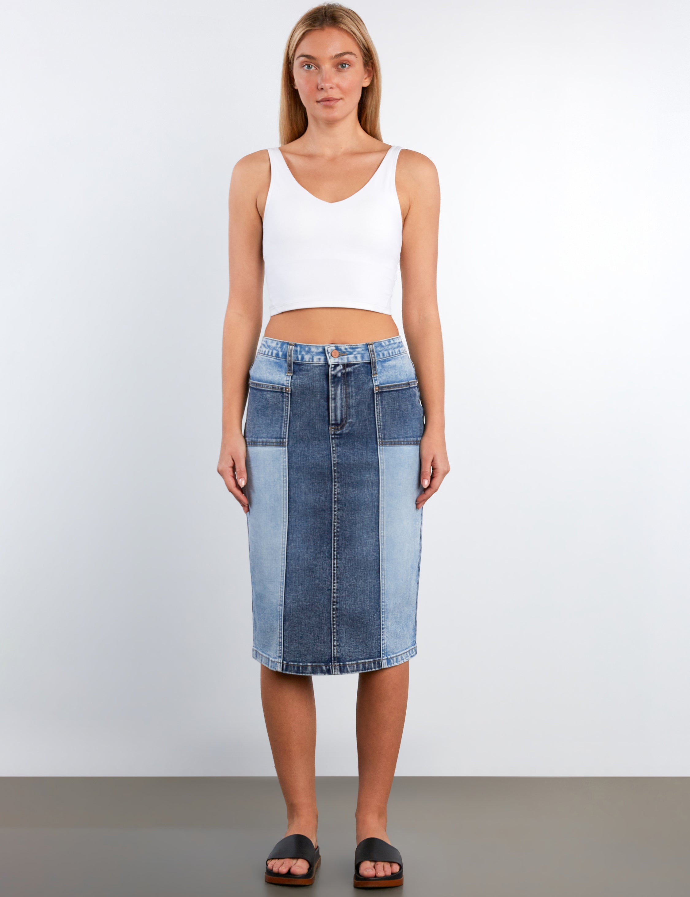 Woman wearing a white tank top and blue denim skirt on a plain background