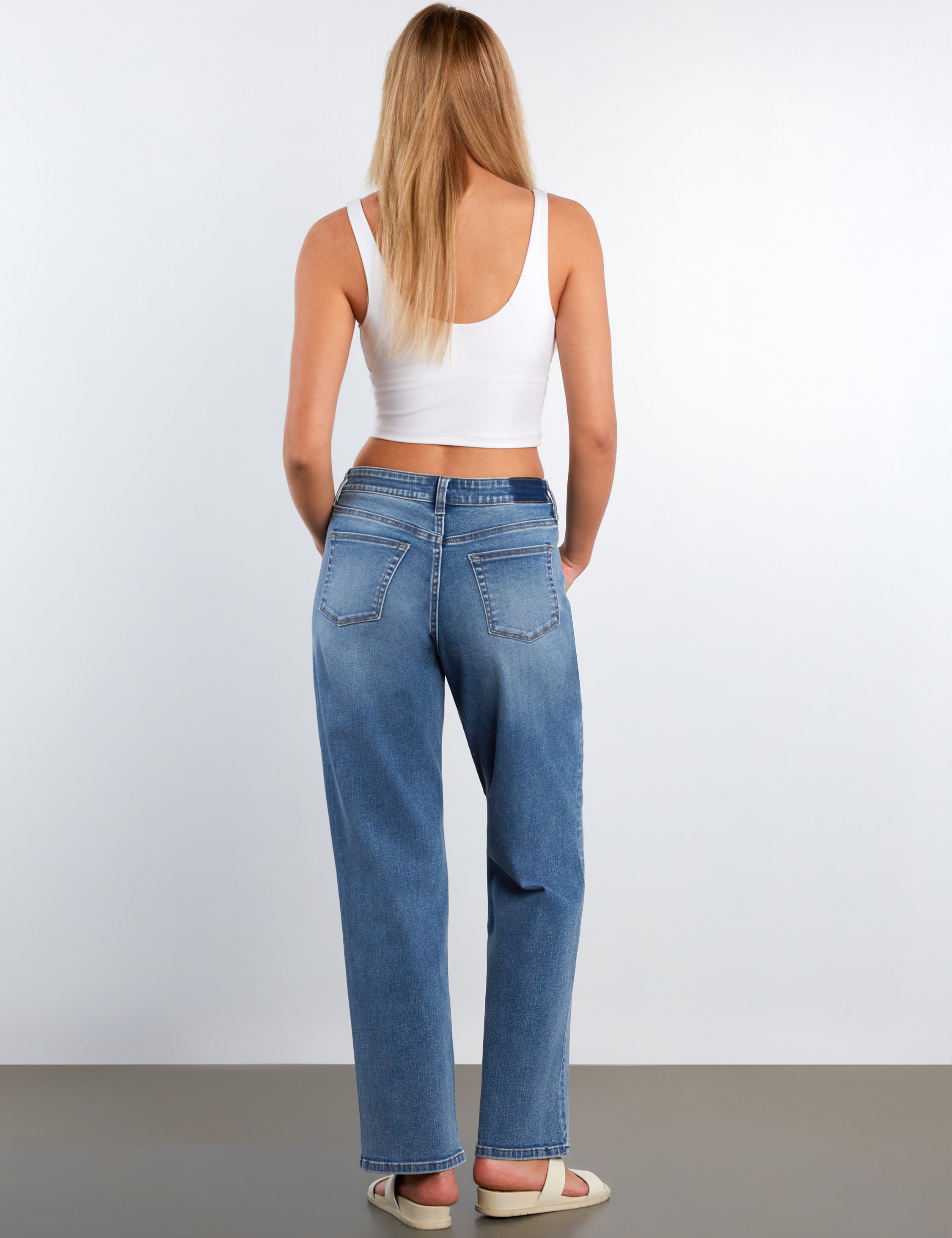 Person wearing blue jeans and a white top on a plain background