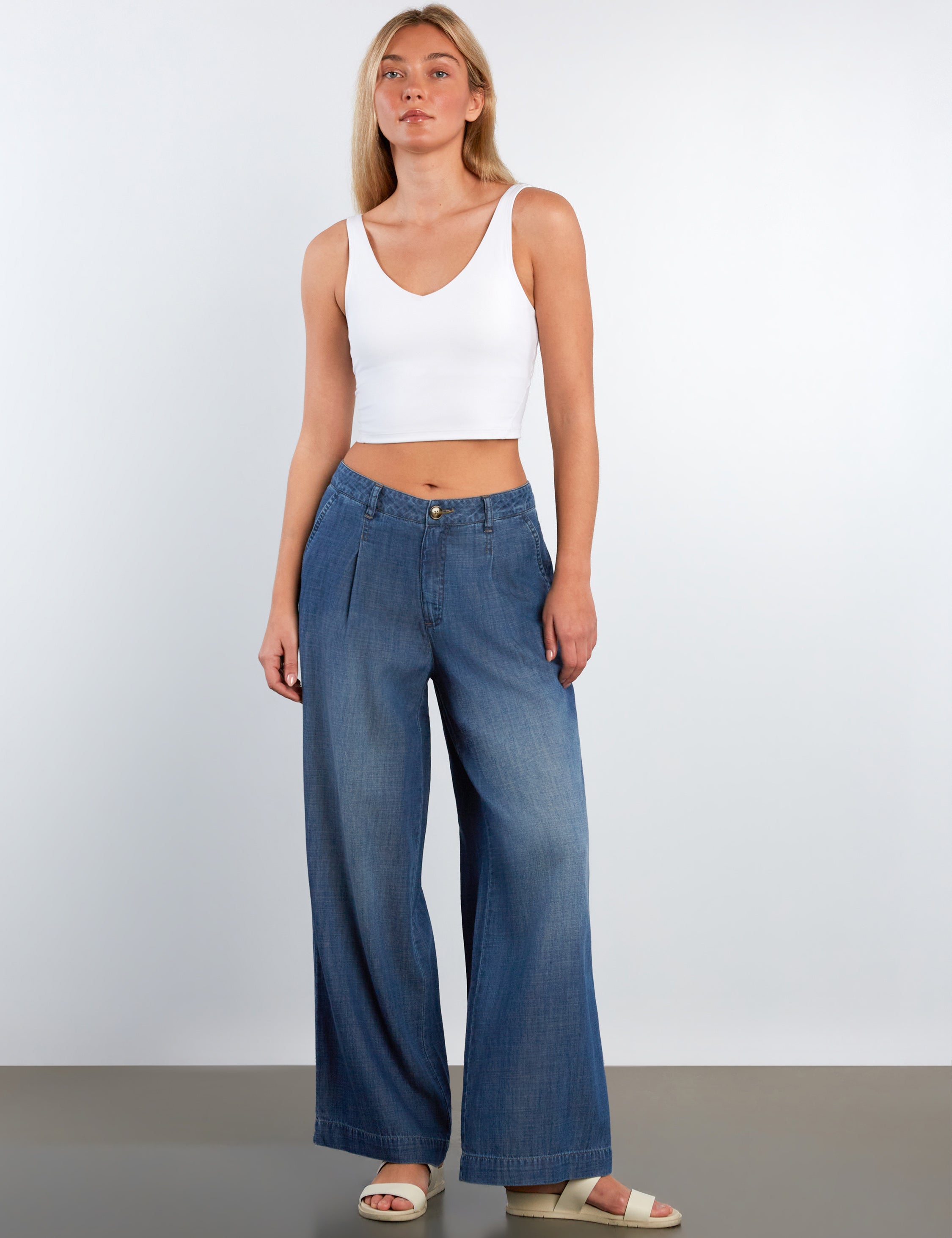 Woman wearing a white tank top and blue jeans against a plain background