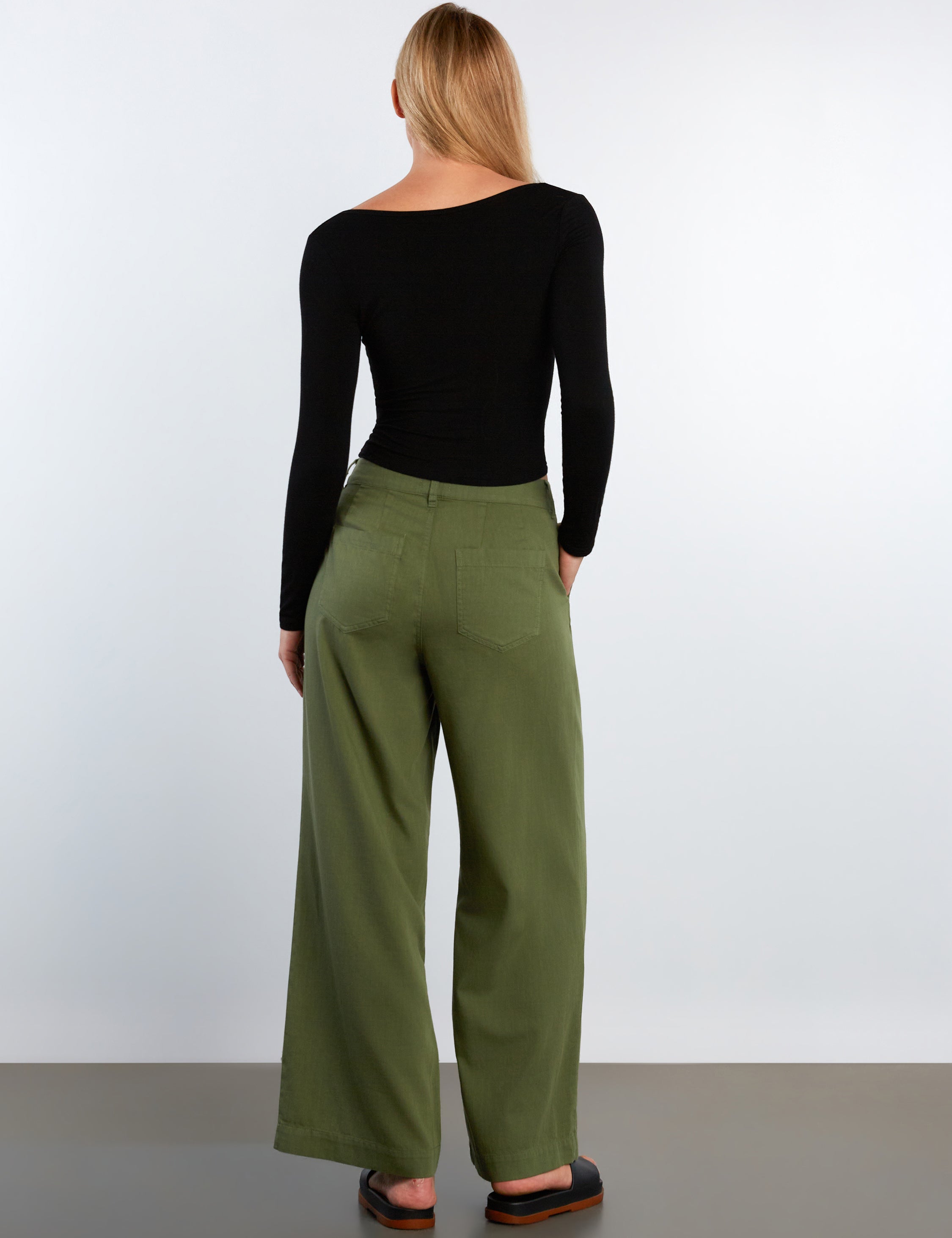 Person wearing a black long-sleeve top and green pants against a white background