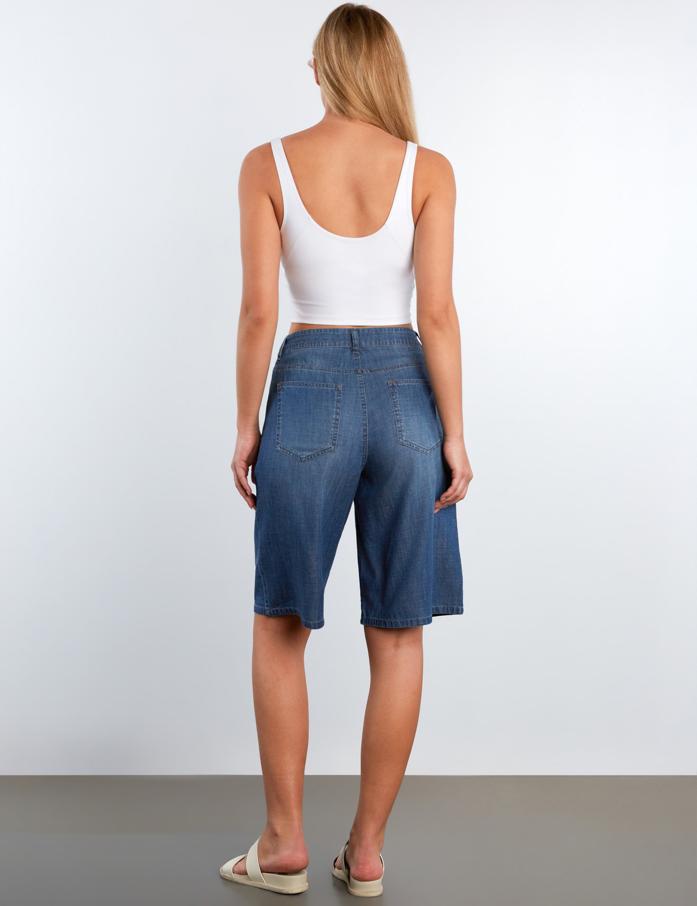 Woman wearing blue denim shorts and a white tank top on a plain background