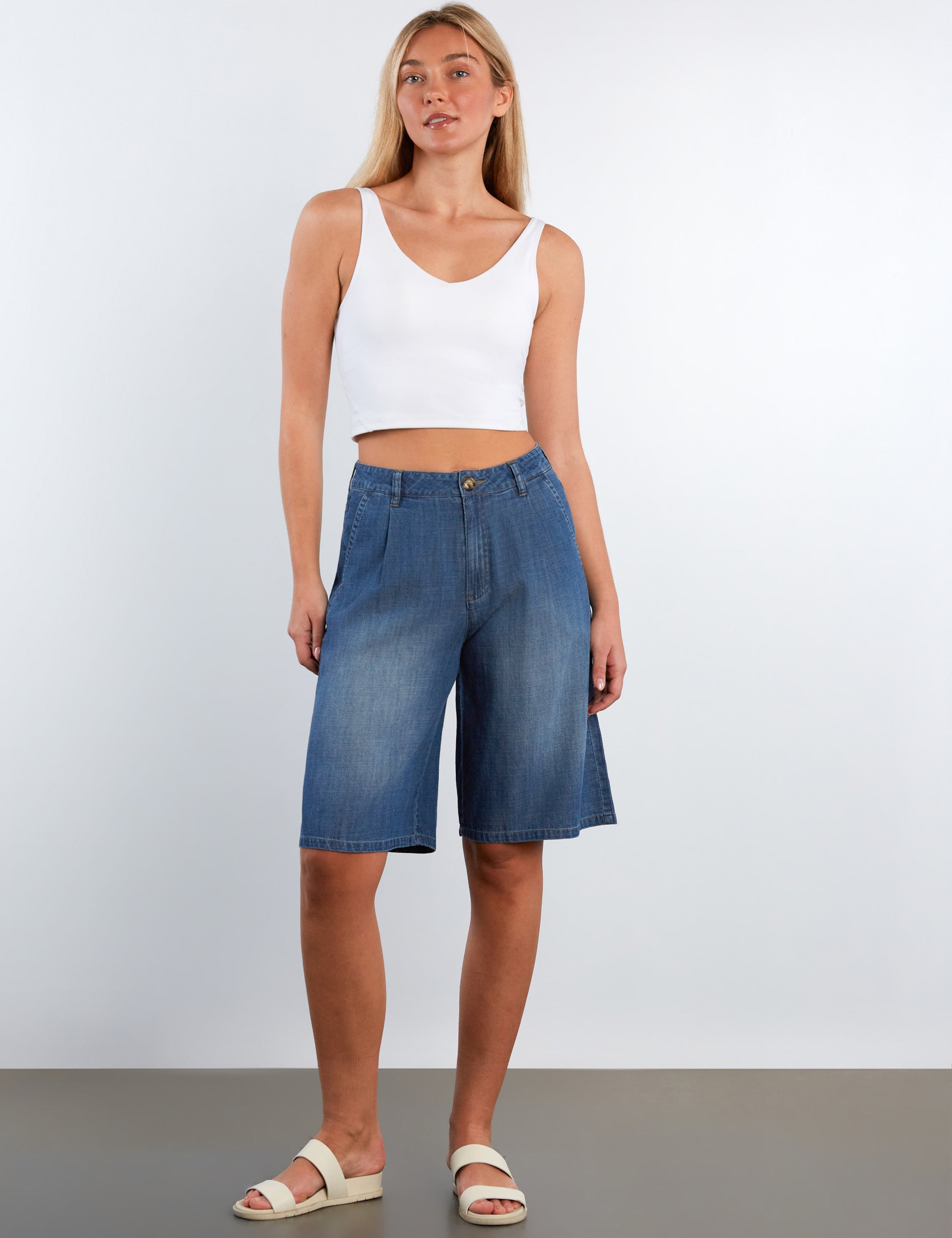 Woman wearing blue denim shorts and a white tank top on a plain background