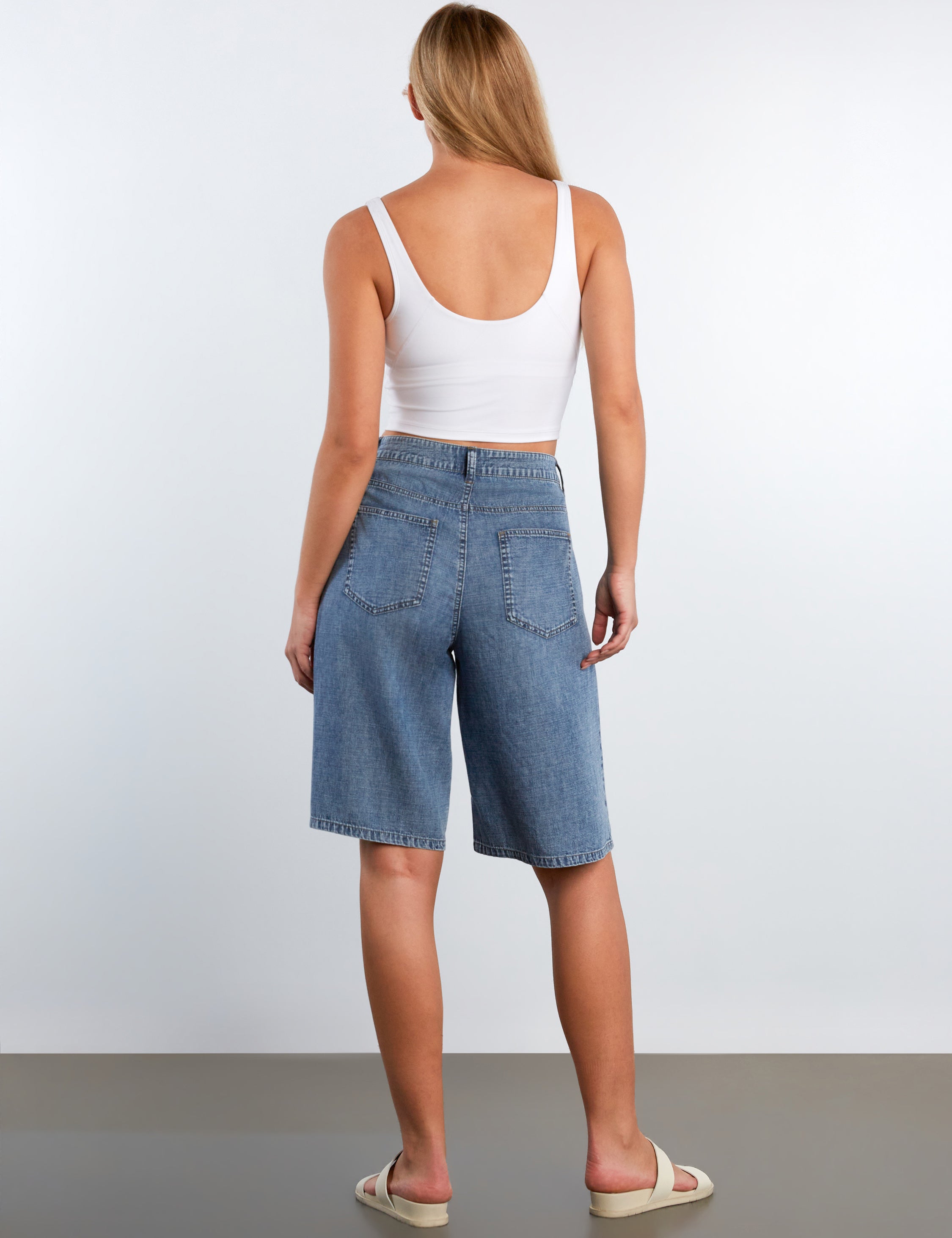 Woman wearing blue denim shorts and a white tank top on a plain background