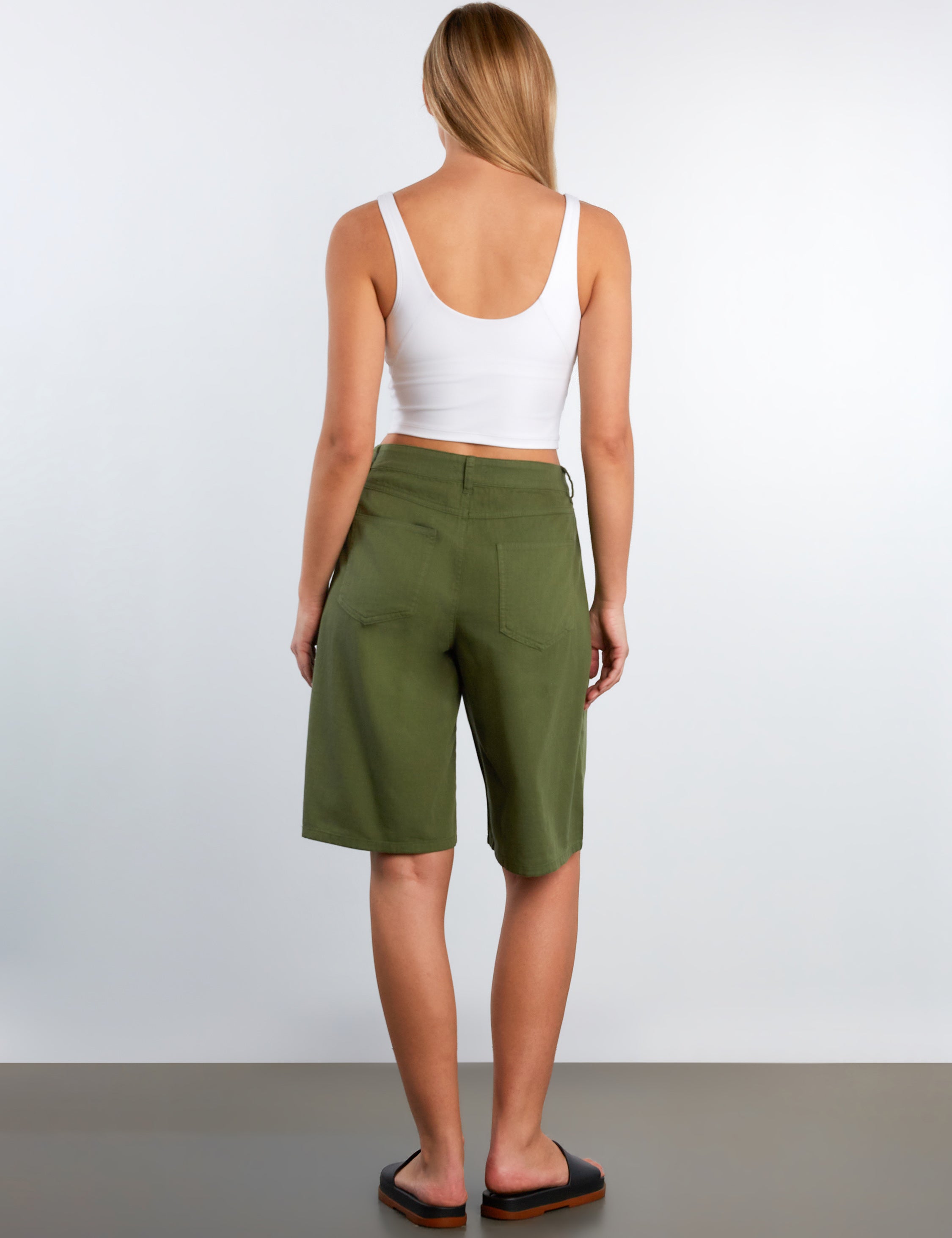 Woman wearing green shorts and a white top on a plain background