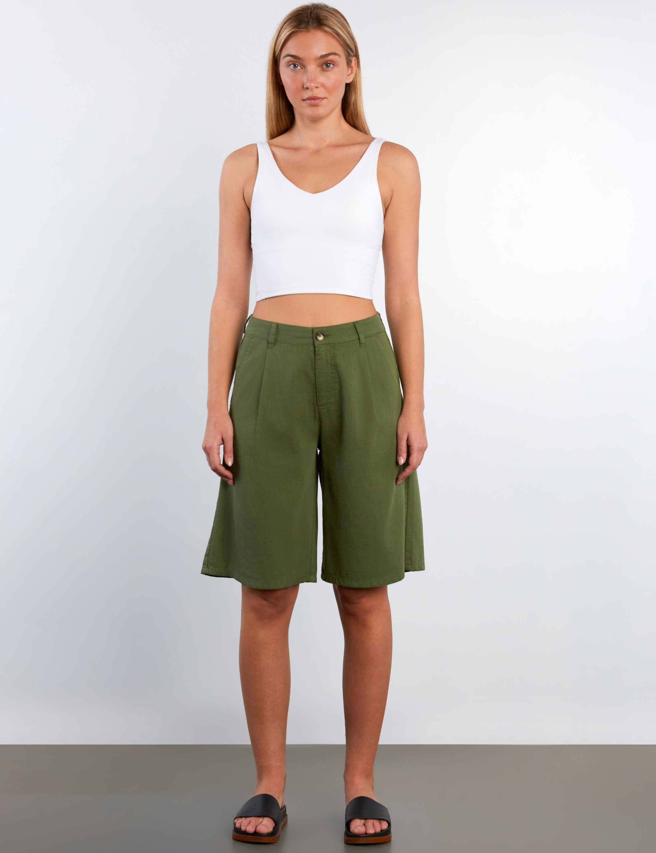 Woman wearing a white tank top and green shorts against a plain background