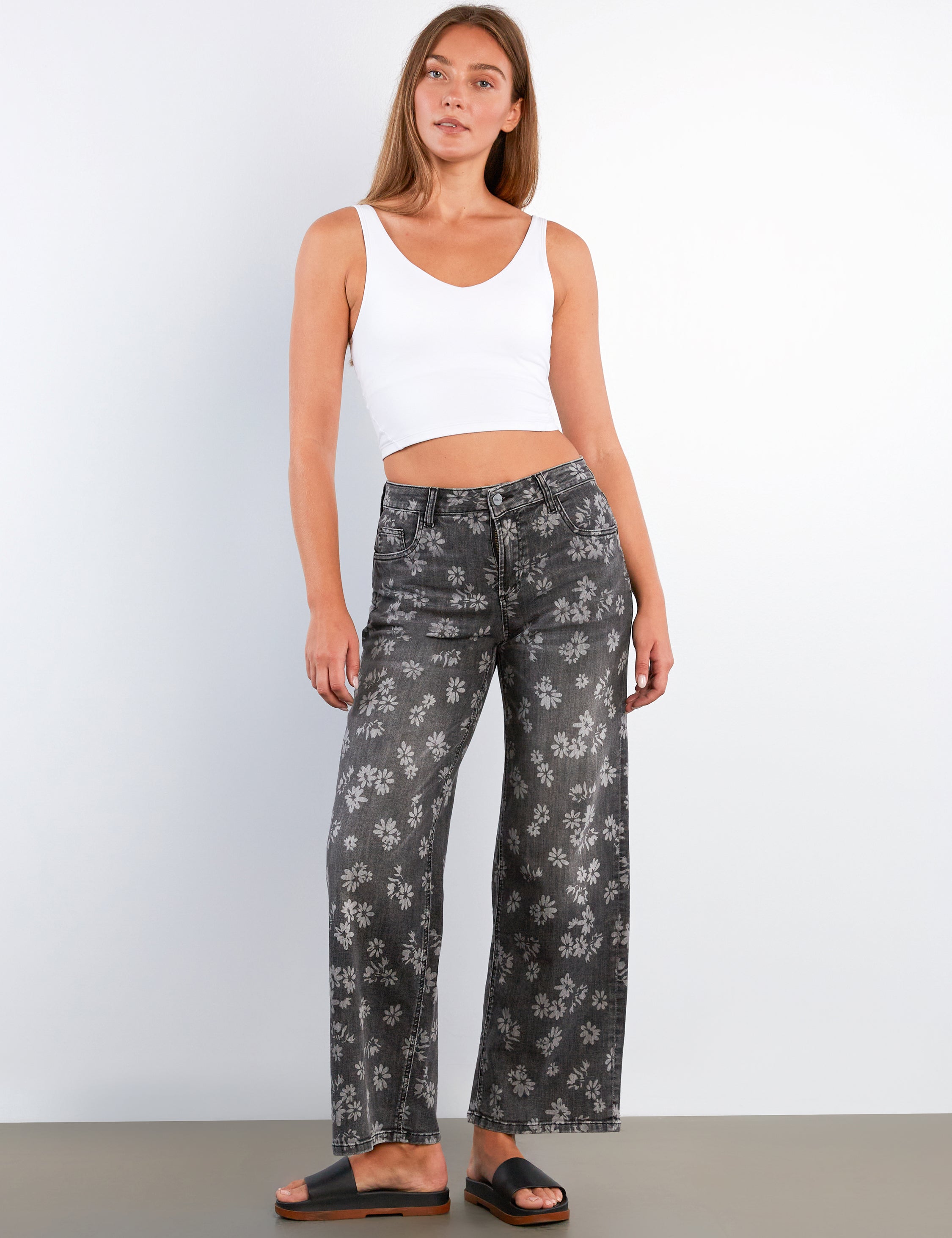Woman wearing a white tank top and black floral pants against a white background