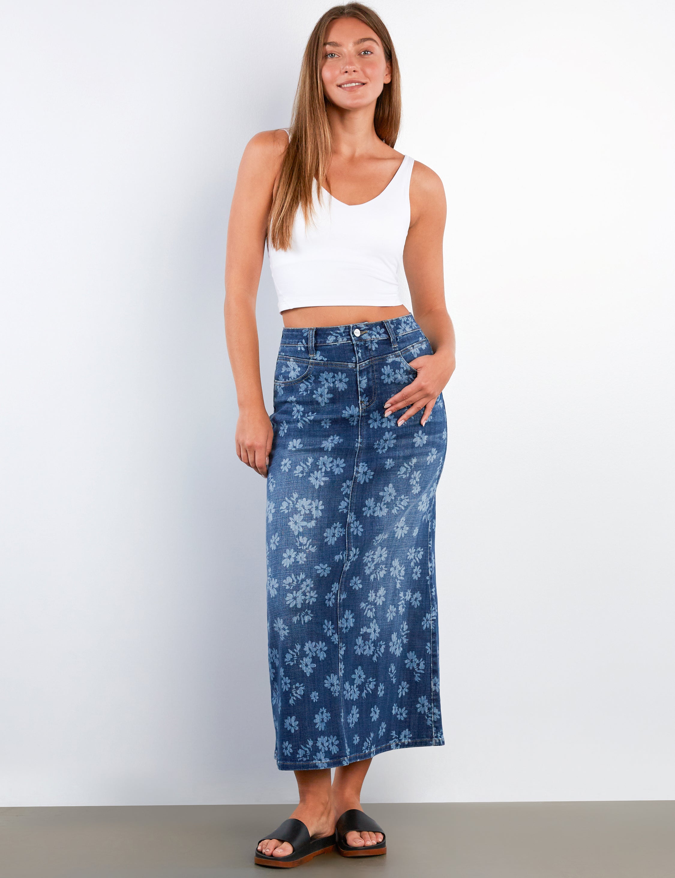 Woman wearing a white tank top and blue floral skirt against a white background