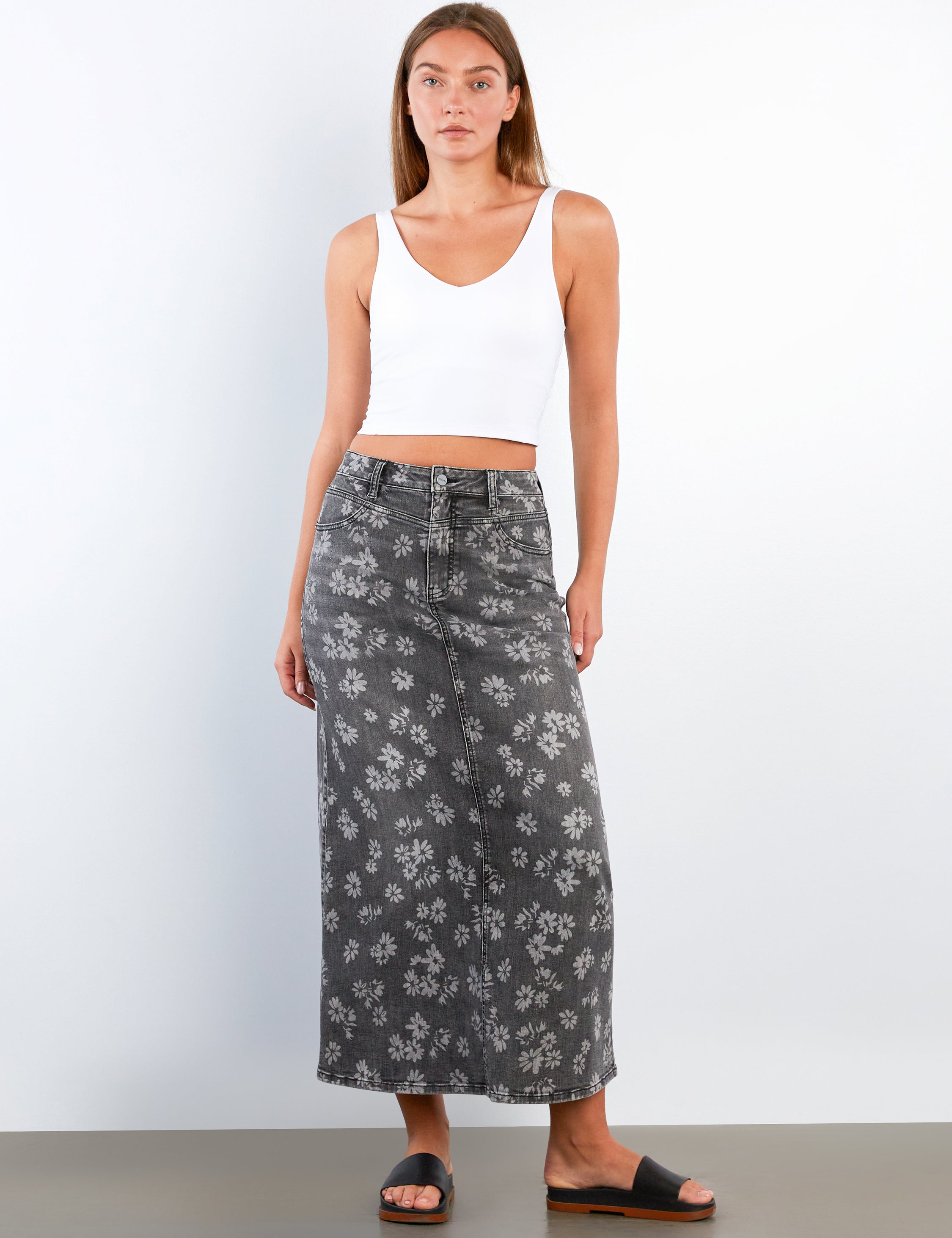 Woman wearing a white tank top and gray floral skirt on a white background