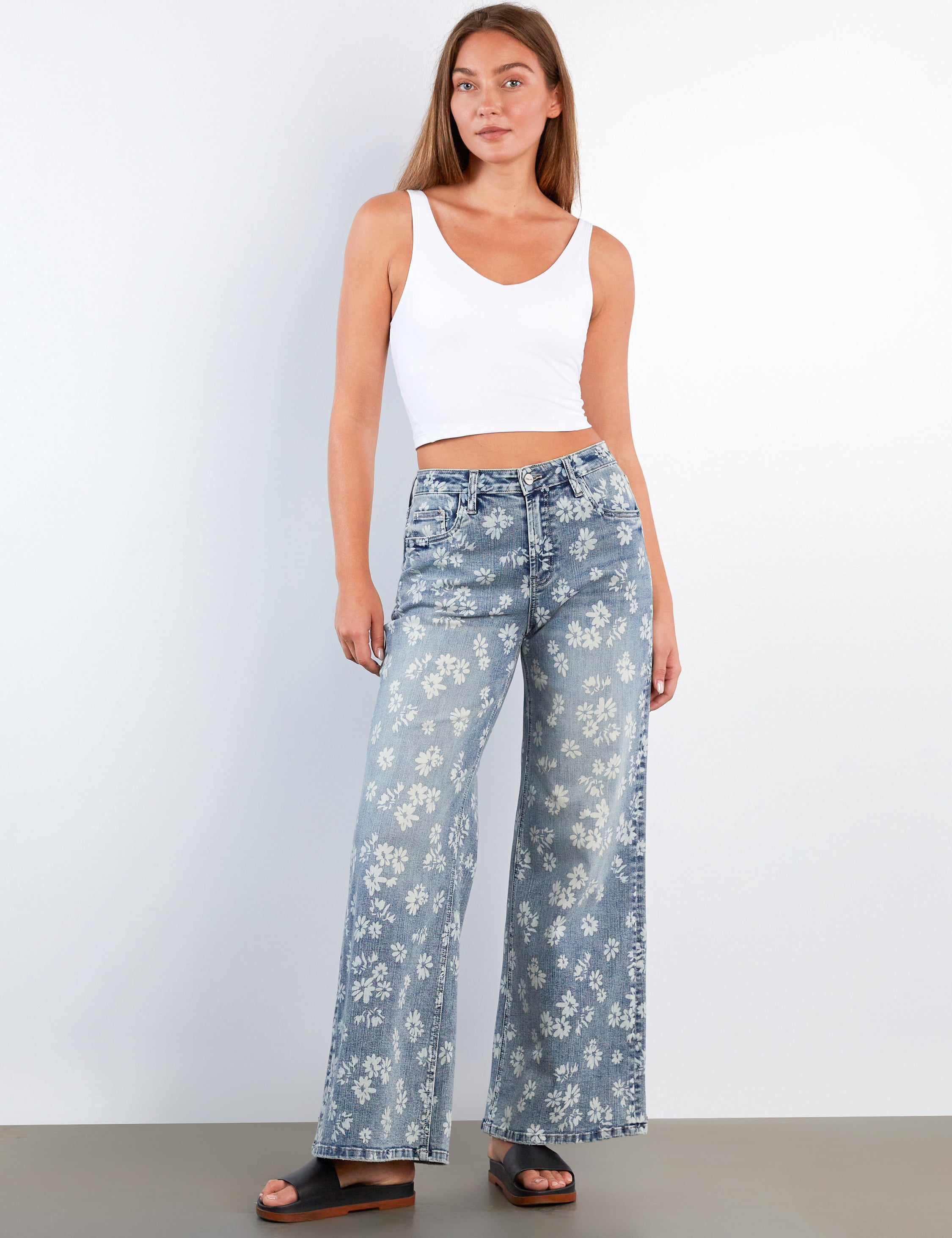 Woman wearing a white tank top and blue floral pants against a white background