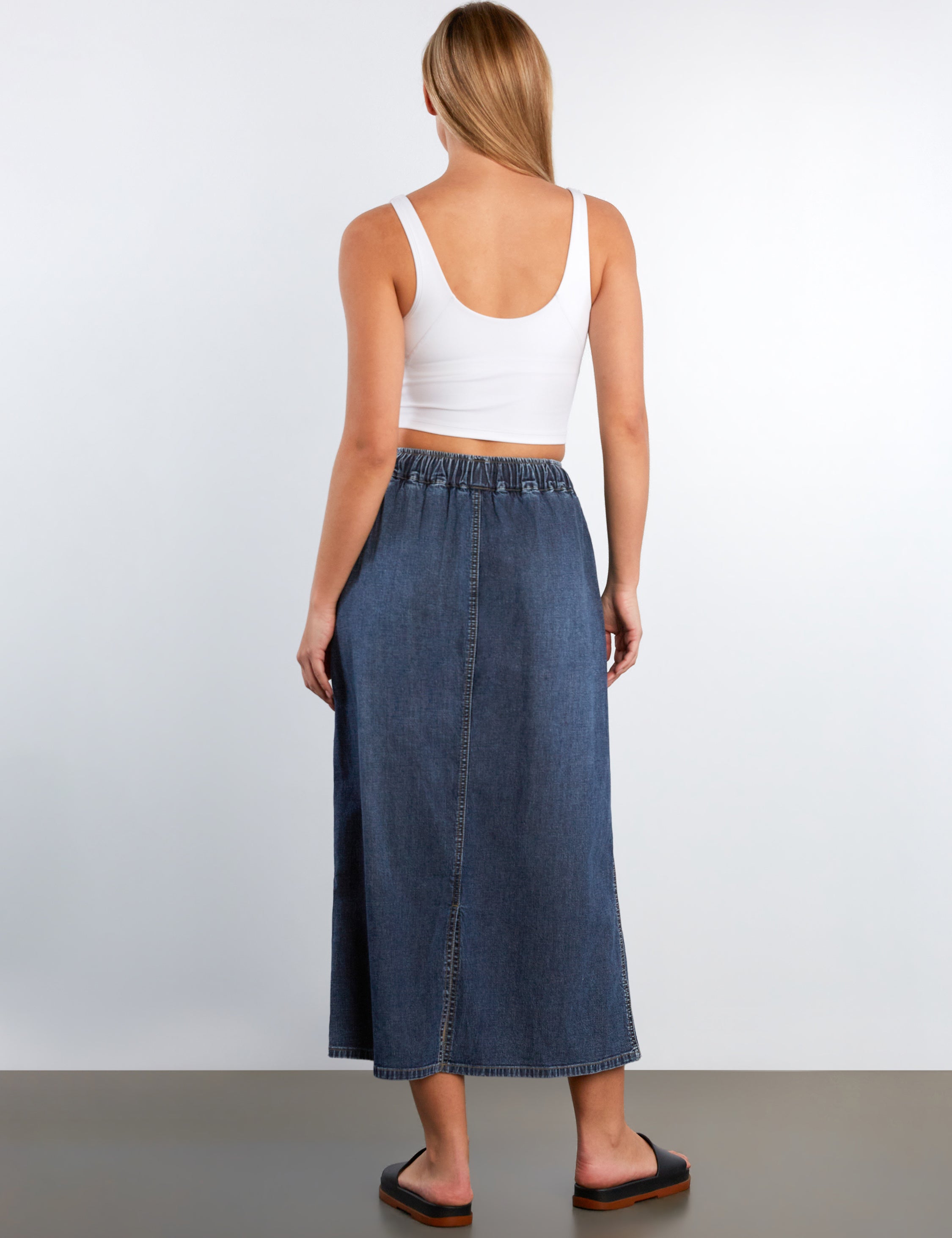 Woman wearing a white tank top and blue denim skirt on a plain background