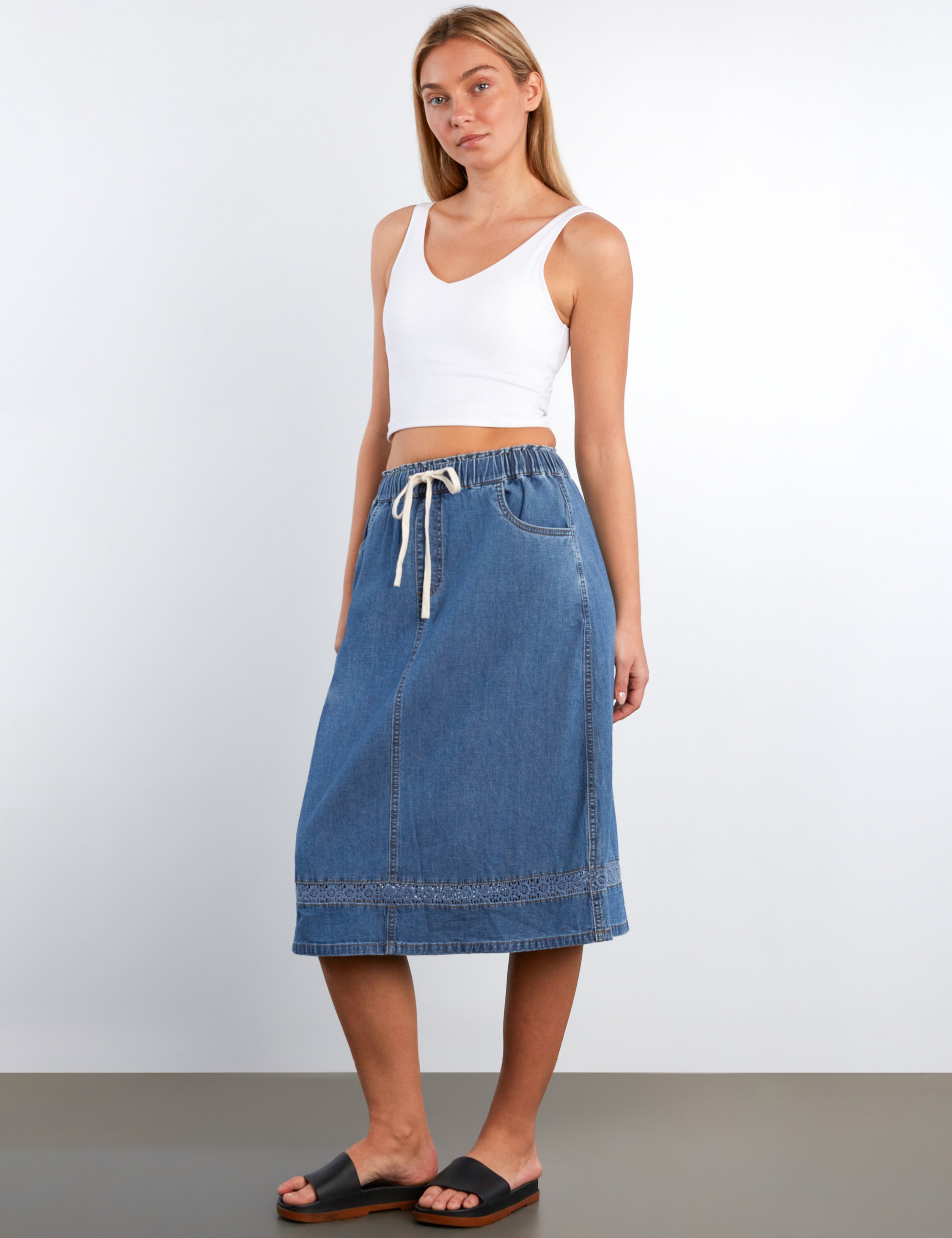 Woman wearing a white tank top and blue denim skirt on a plain background