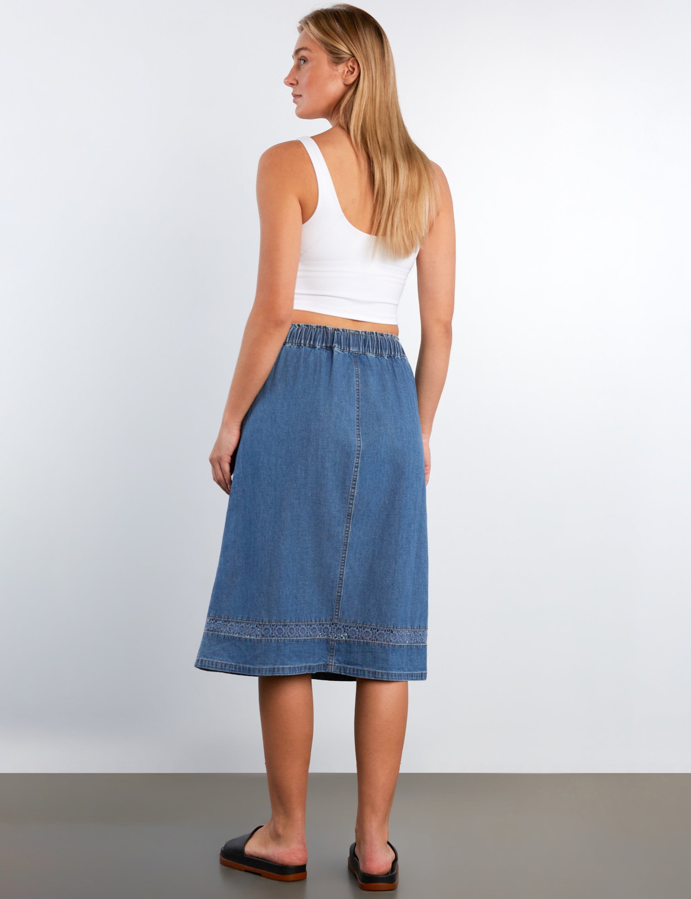 Woman wearing a white tank top and blue denim skirt against a plain background