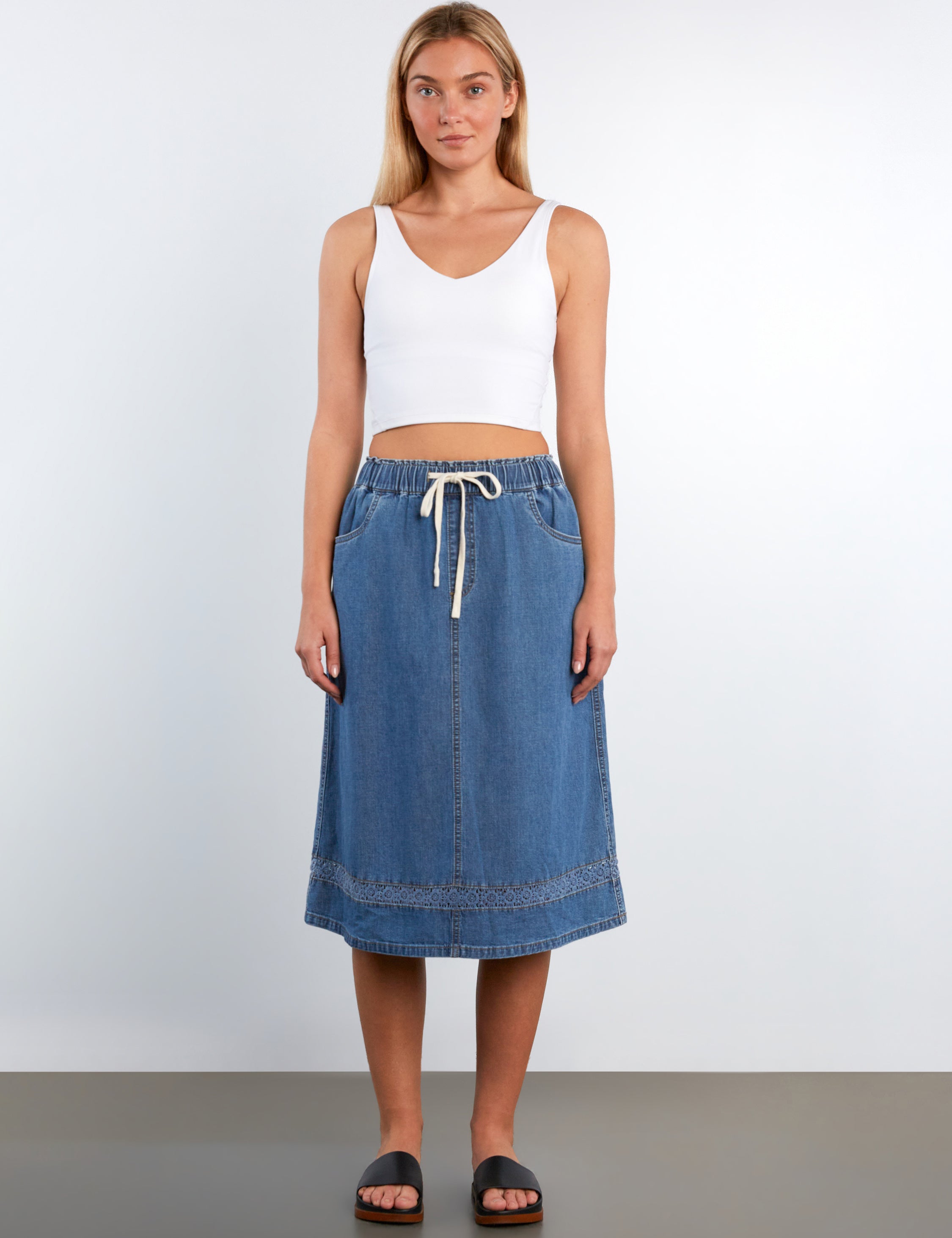Woman wearing a white tank top and blue denim skirt on a plain background