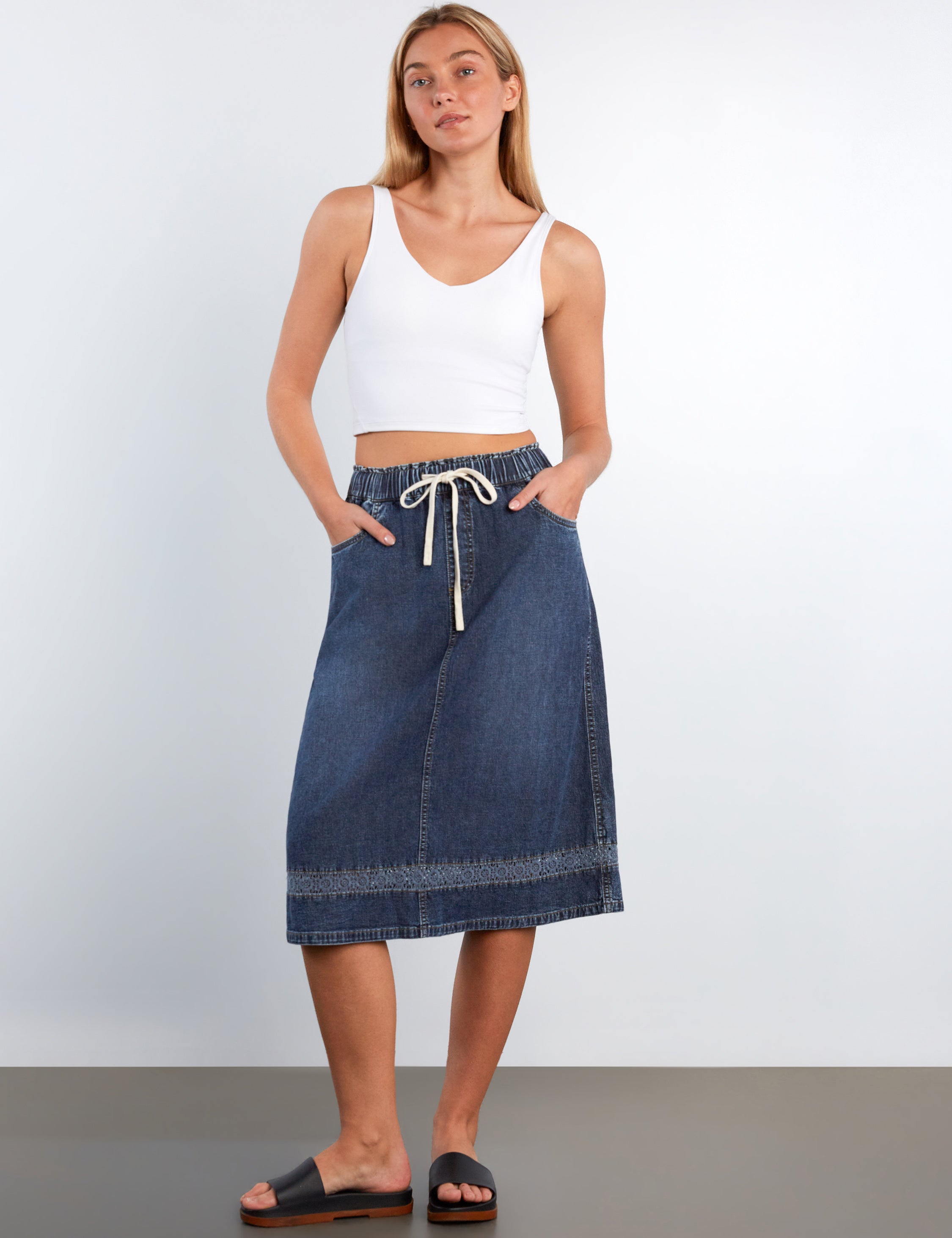 Woman wearing a white tank top and blue denim skirt on a plain background