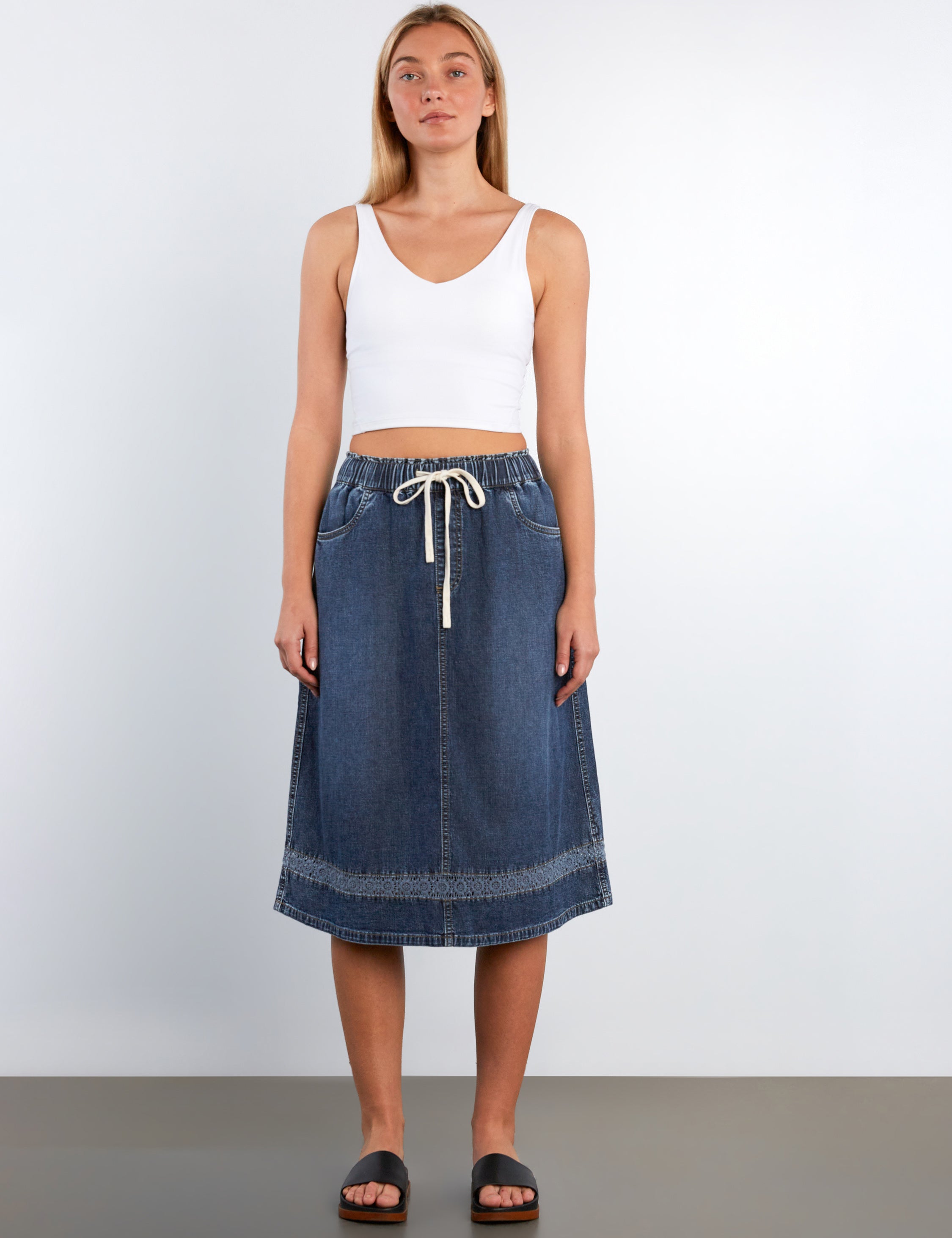 Woman wearing a white tank top and blue denim skirt on a plain background