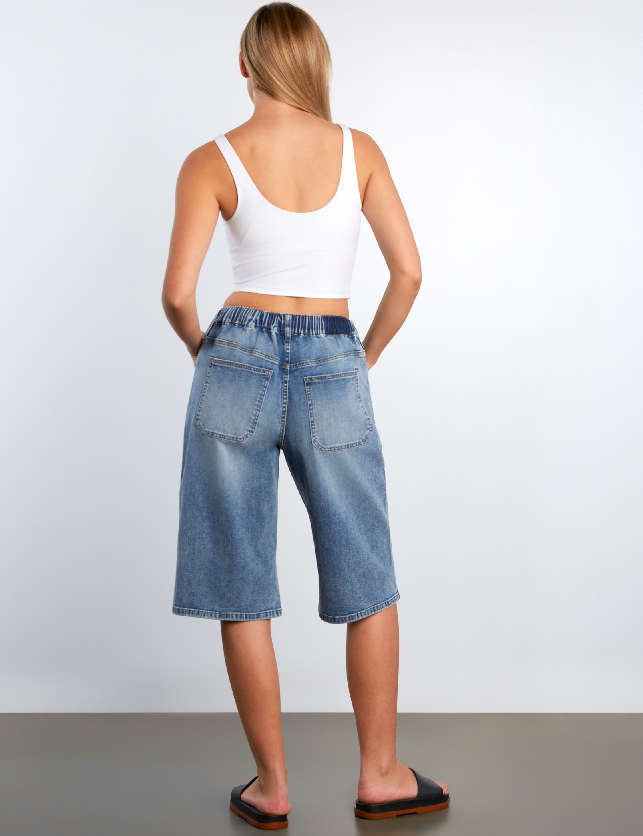Person wearing a white tank top and blue denim shorts on a plain background