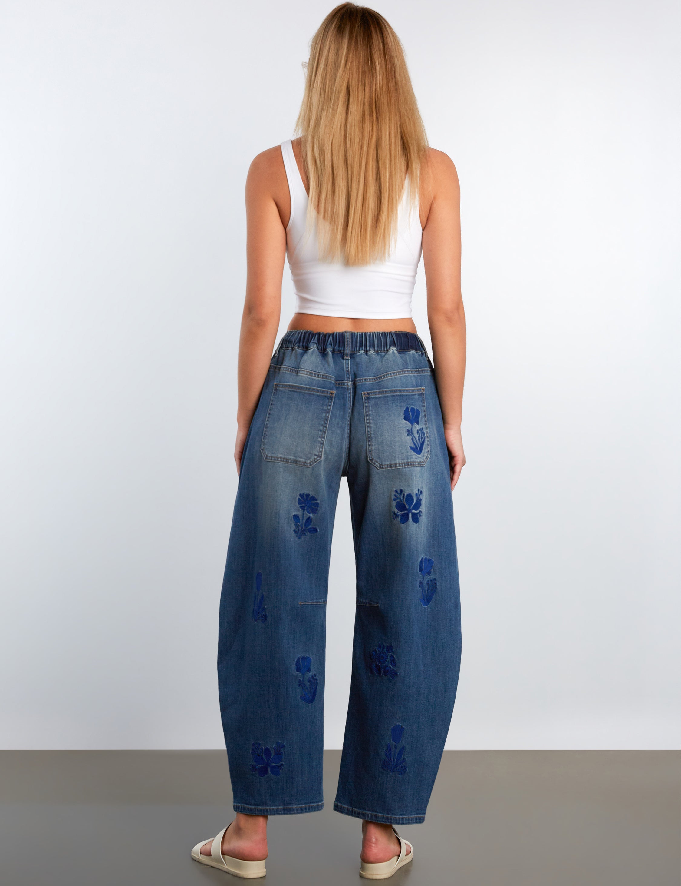 Woman wearing blue distressed wide-leg jeans and a white top on a plain background