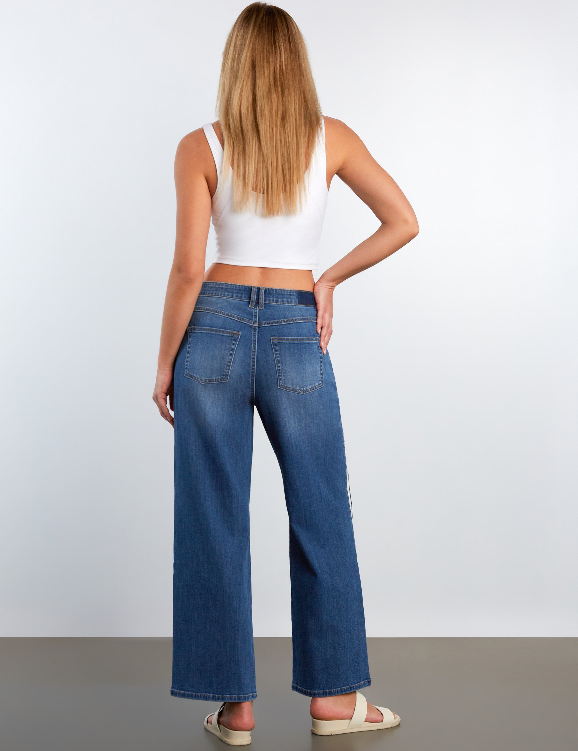 Woman wearing blue jeans and a white top on a plain background