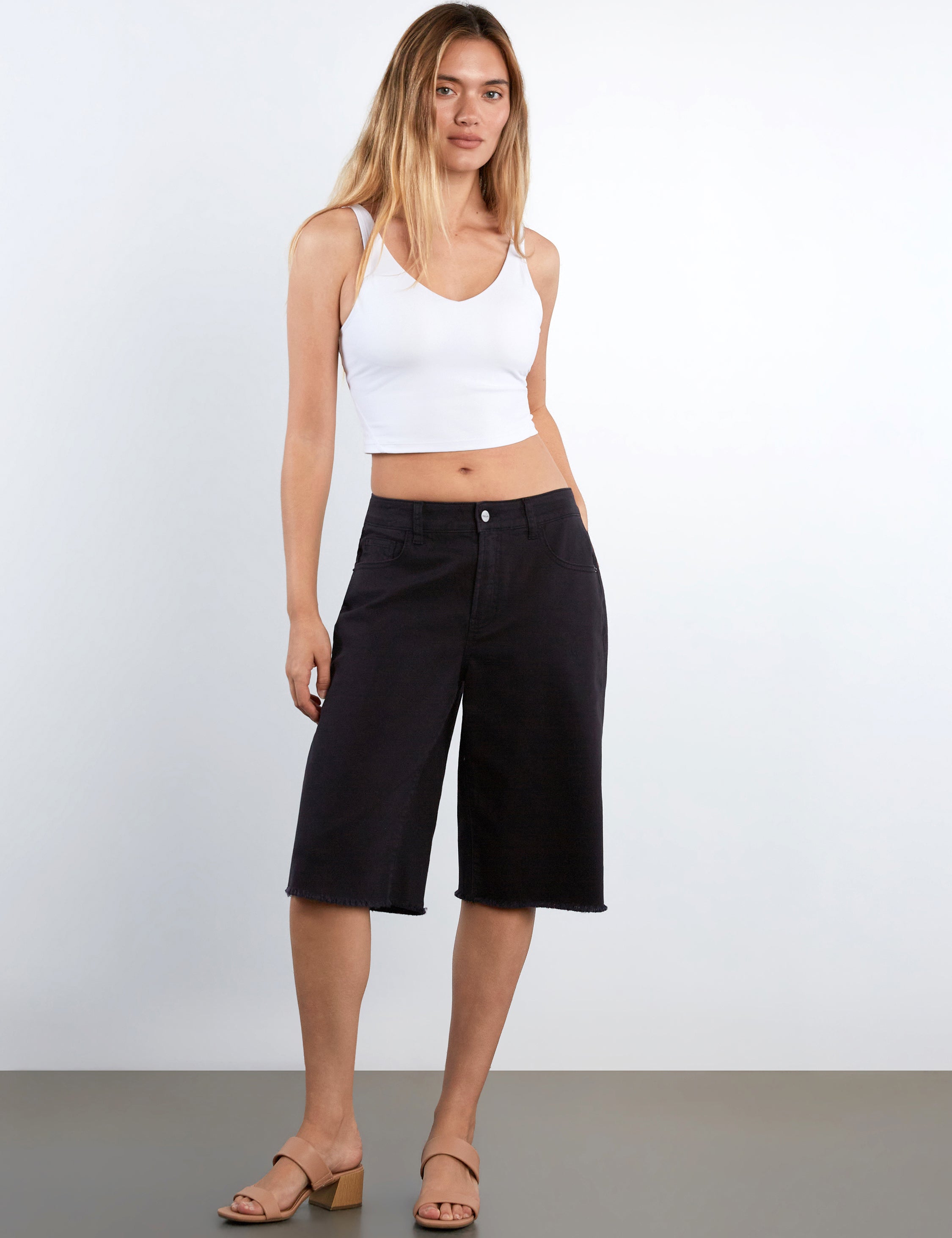 Woman wearing a white tank top and black shorts on a plain background