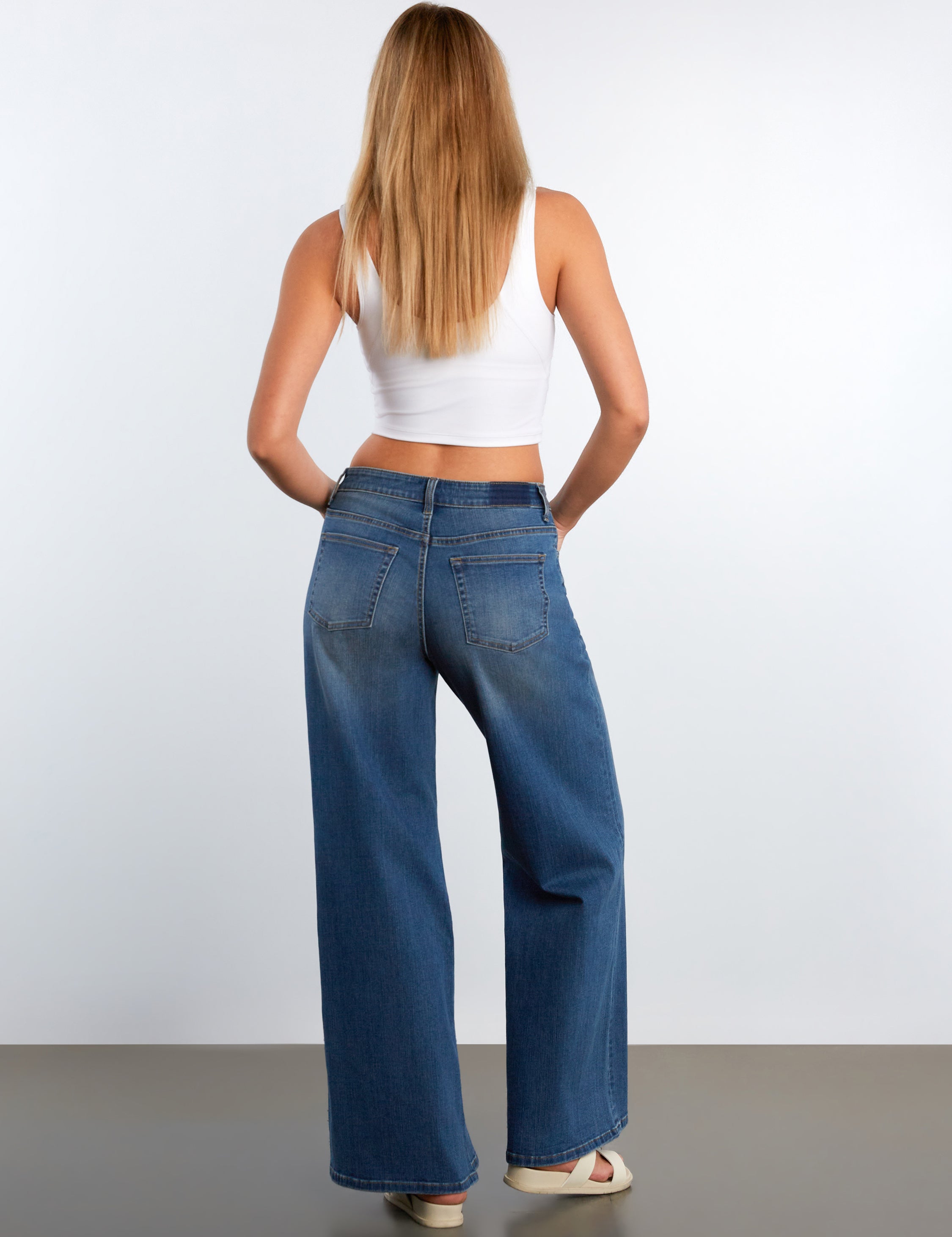 Woman wearing blue jeans and a white top on a plain background