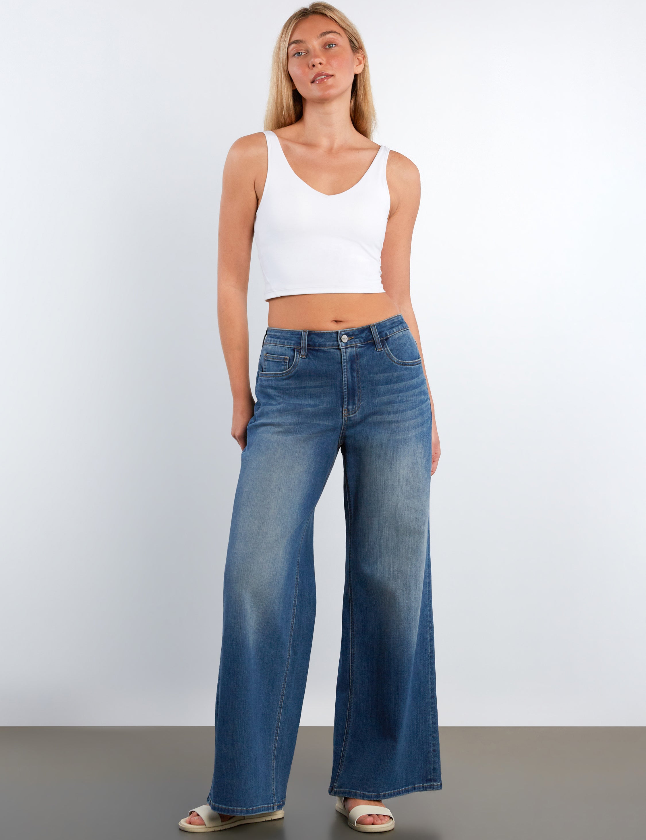 Woman wearing blue jeans and a white top against a plain background