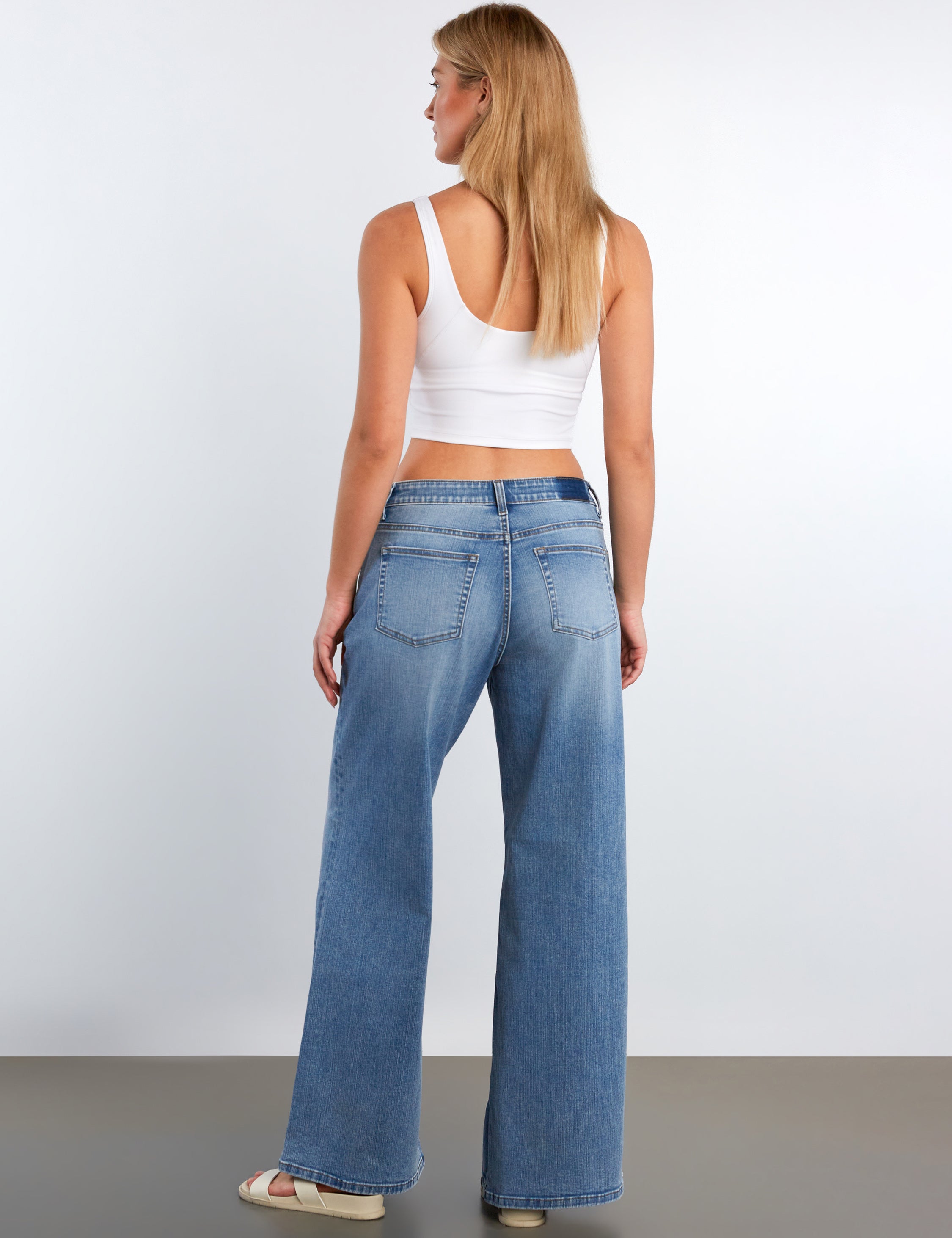 Woman wearing blue jeans and a white top against a plain background