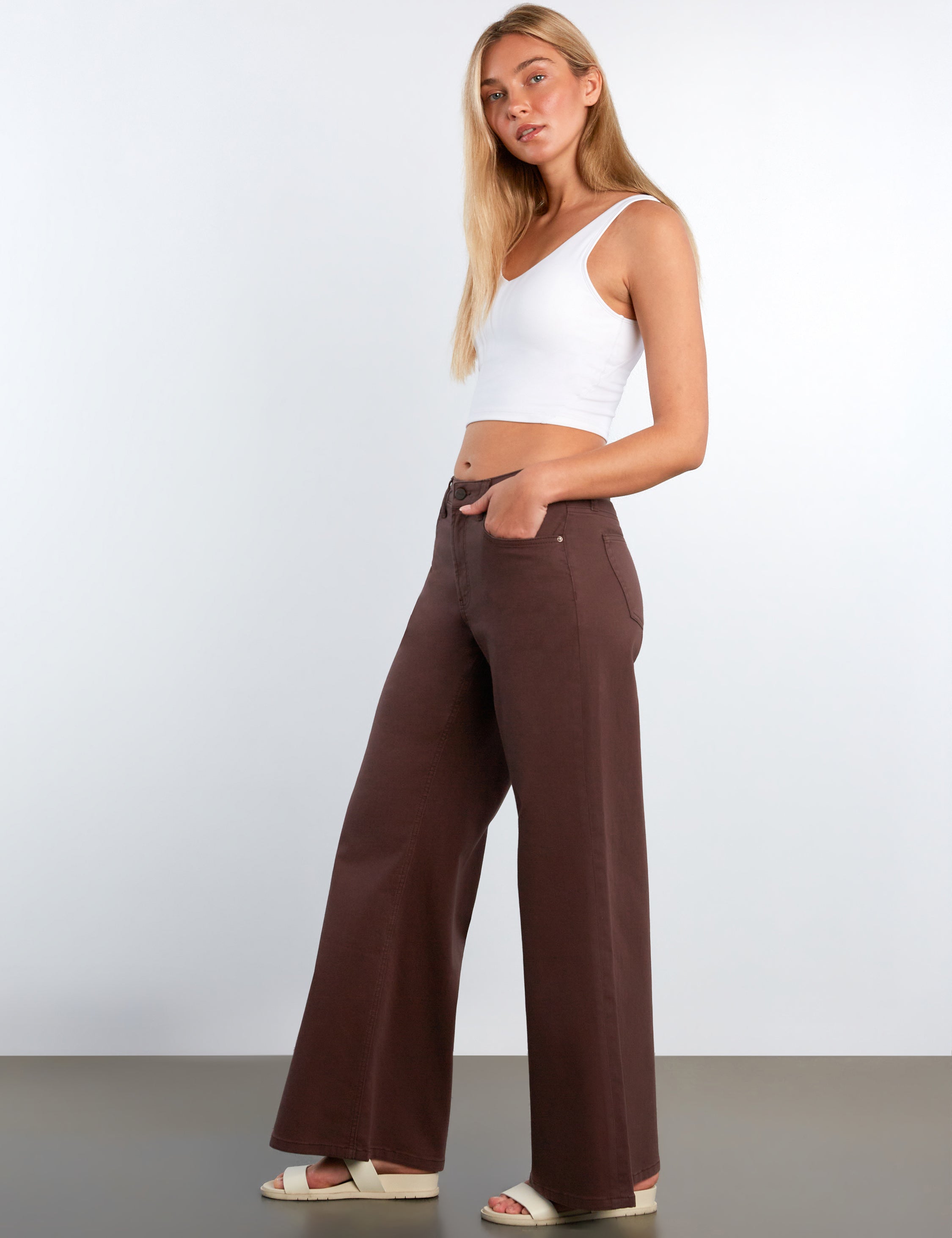 Woman wearing a white tank top and brown wide-leg pants against a white background