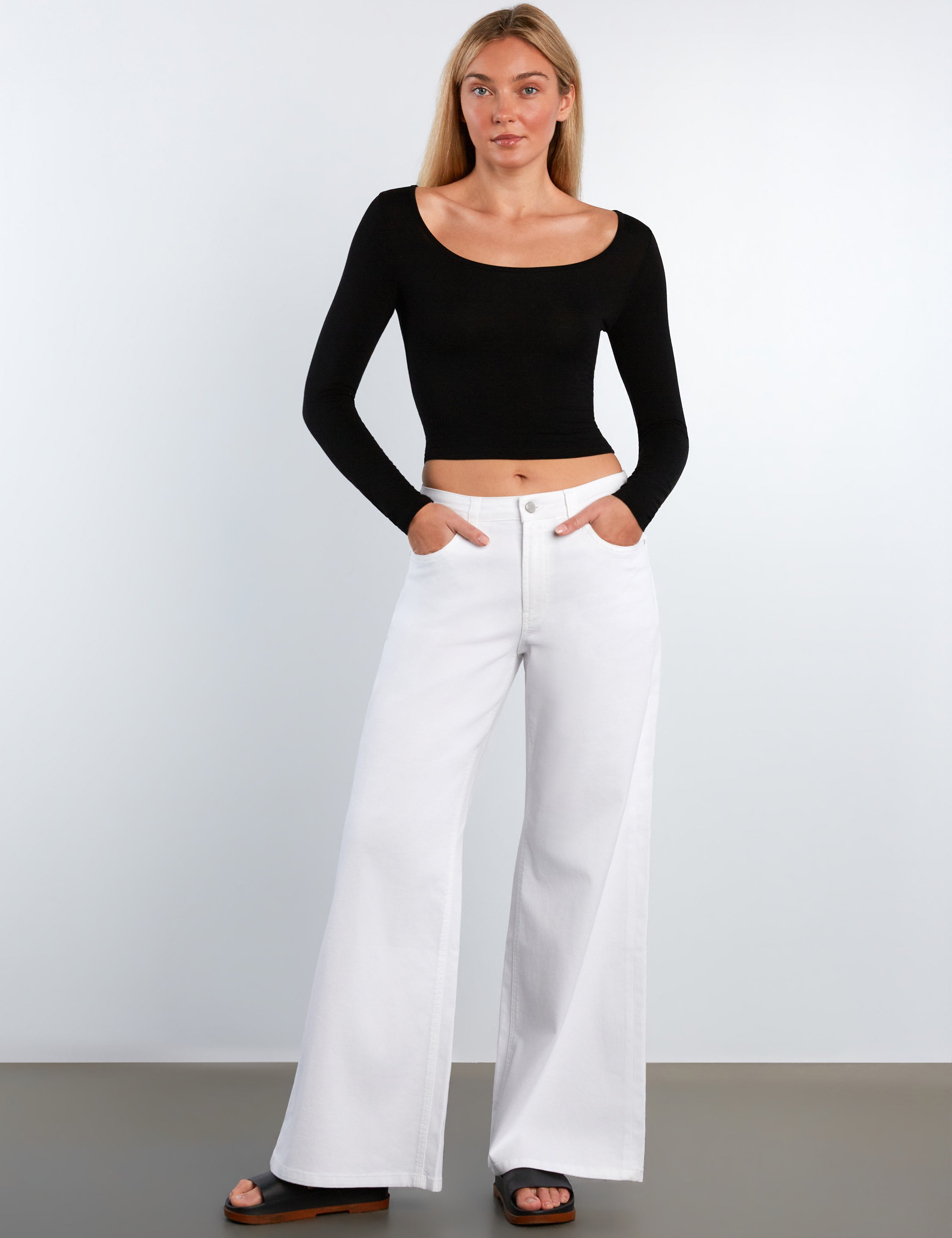 Woman wearing a black long-sleeve top and white wide-leg pants on a plain background