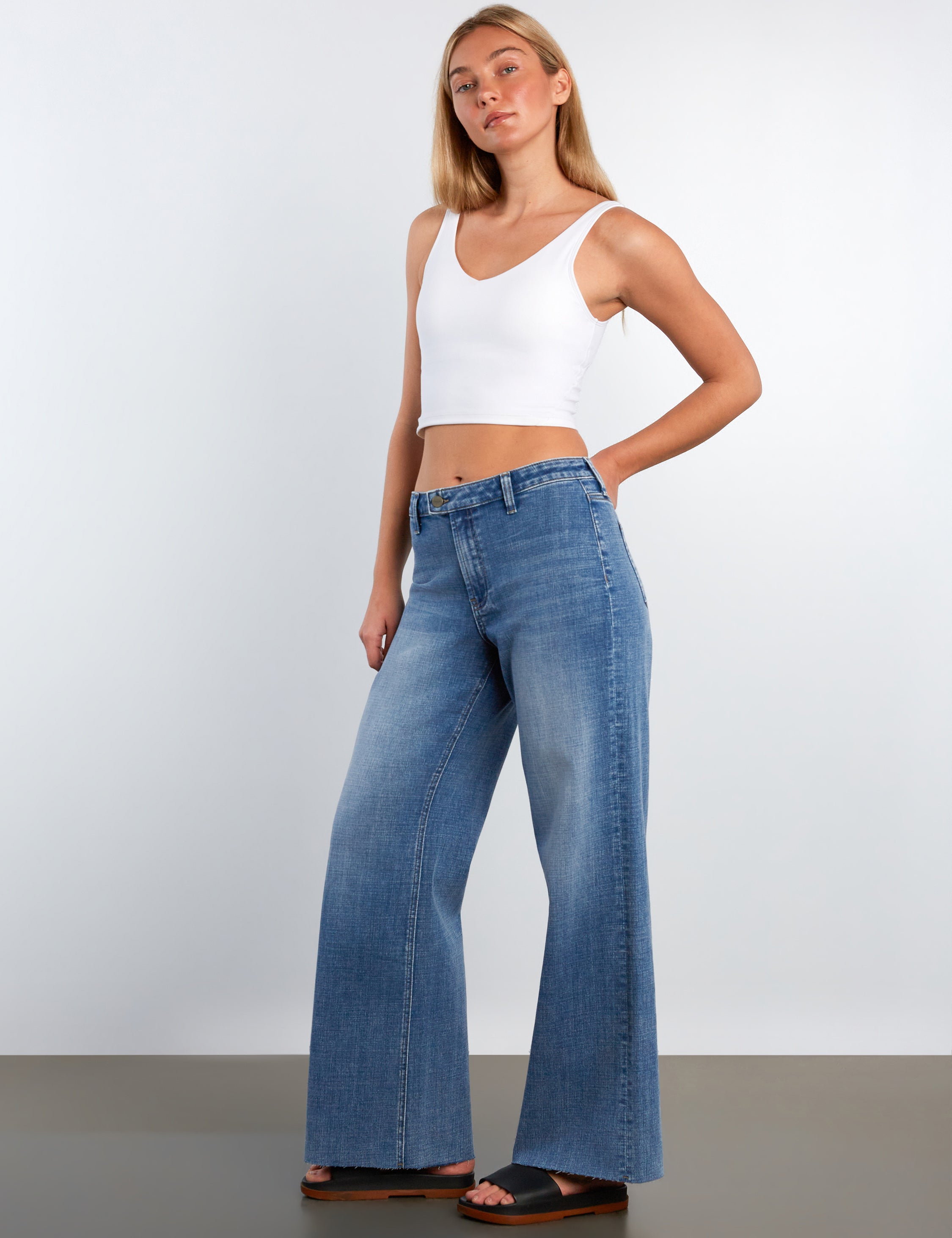Woman wearing a white tank top and blue jeans against a plain background