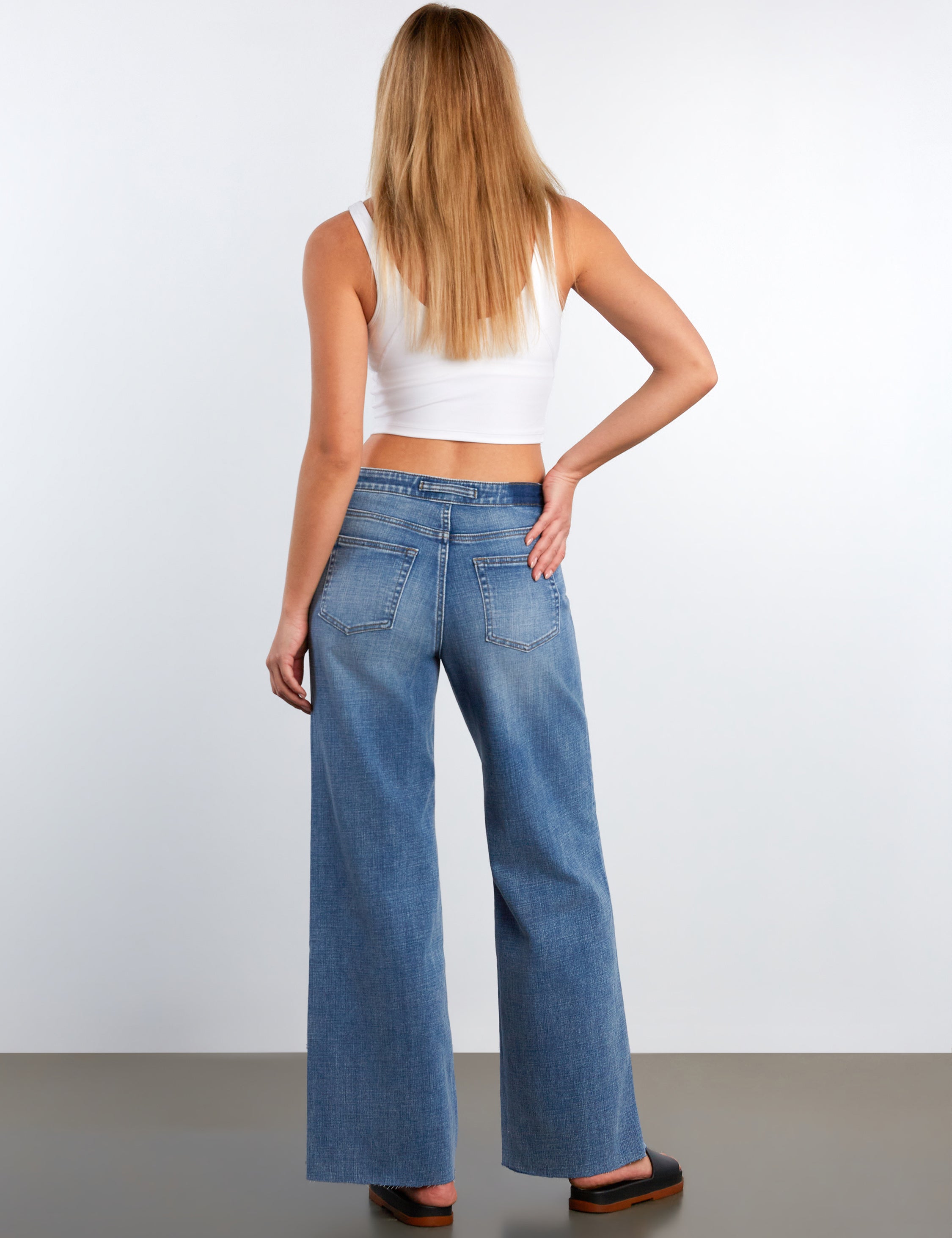 Woman wearing blue jeans and a white top on a plain background