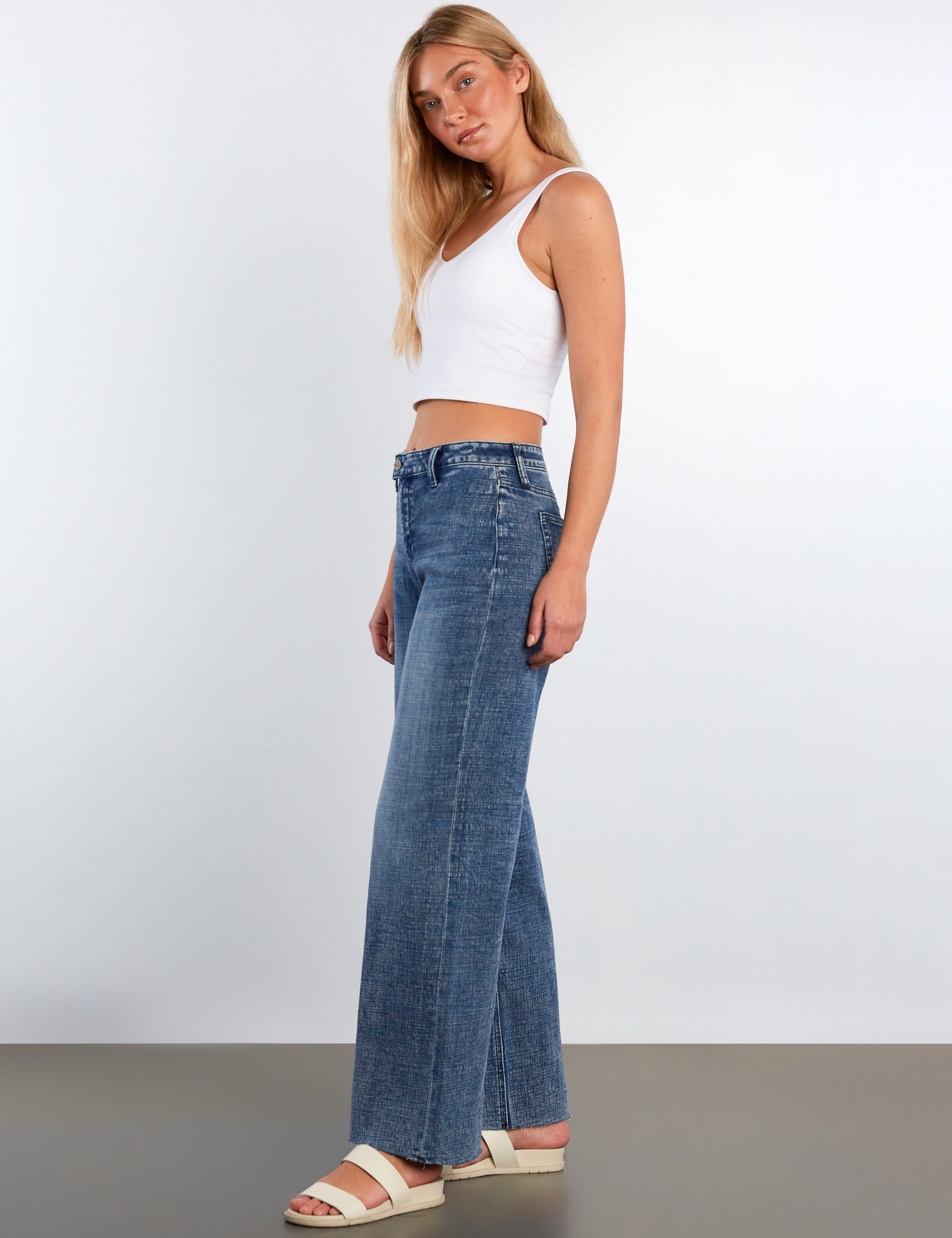 Woman wearing blue jeans and a white top against a plain background