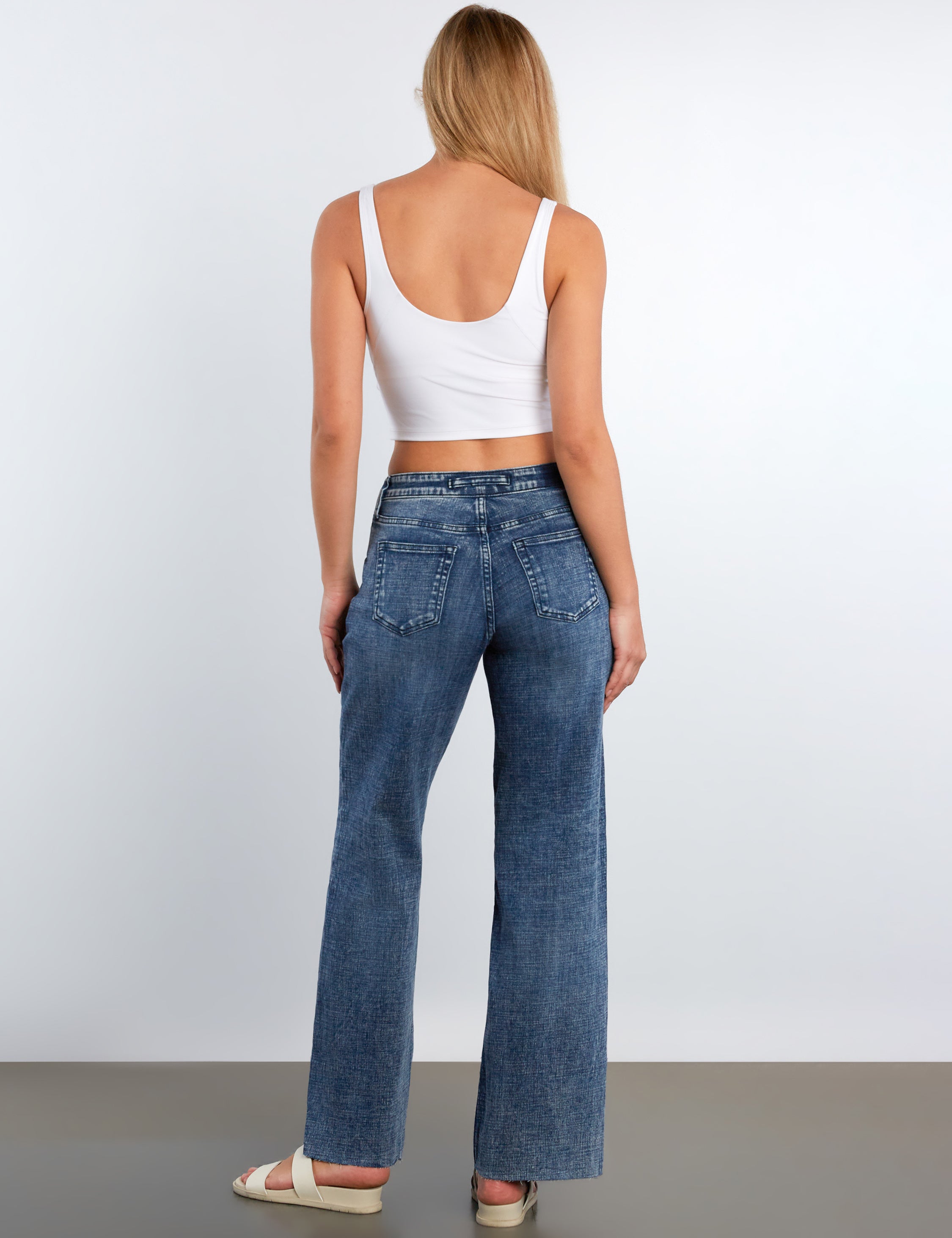 Woman wearing blue jeans and a white top on a plain background