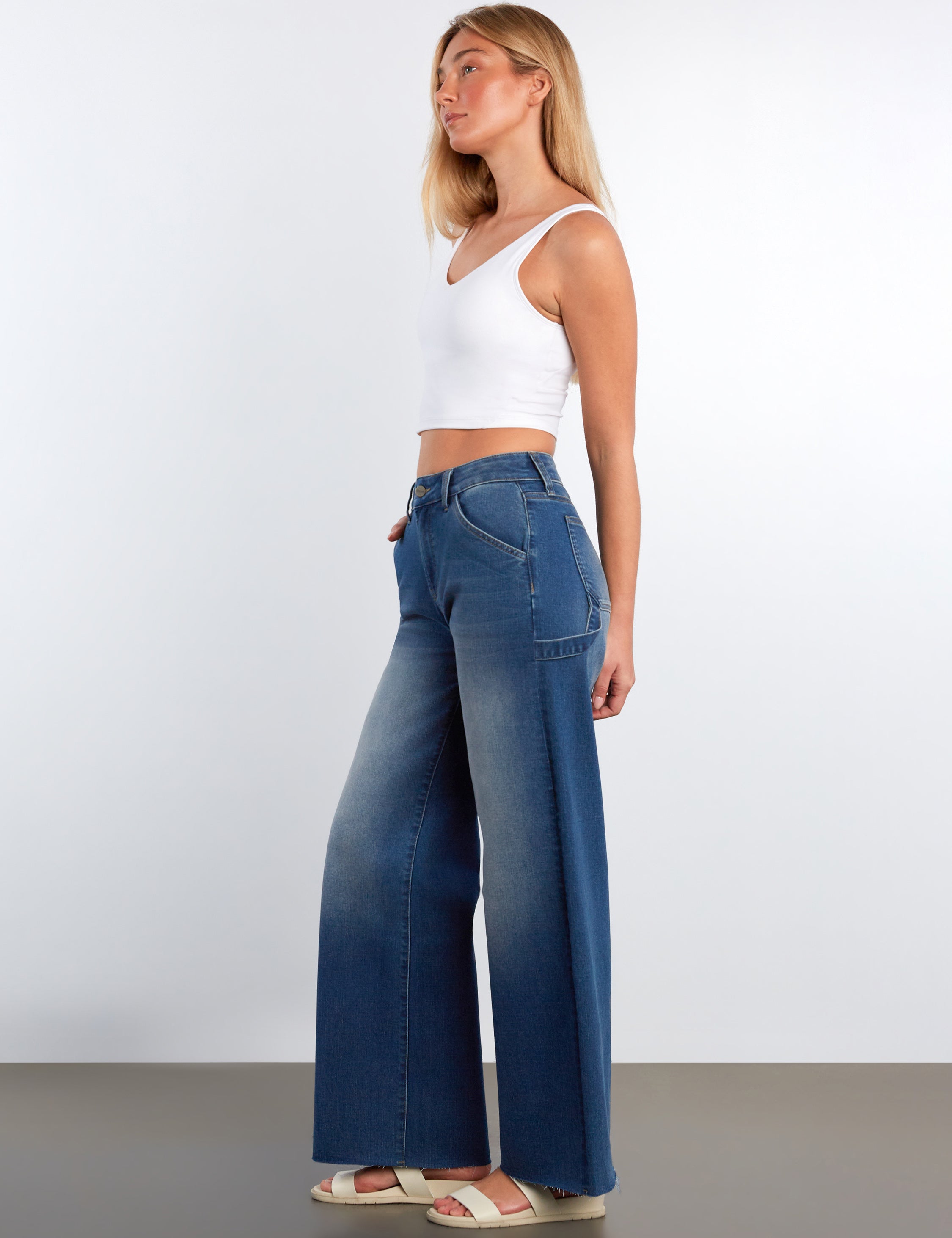 Woman wearing blue jeans and a white top against a plain background
