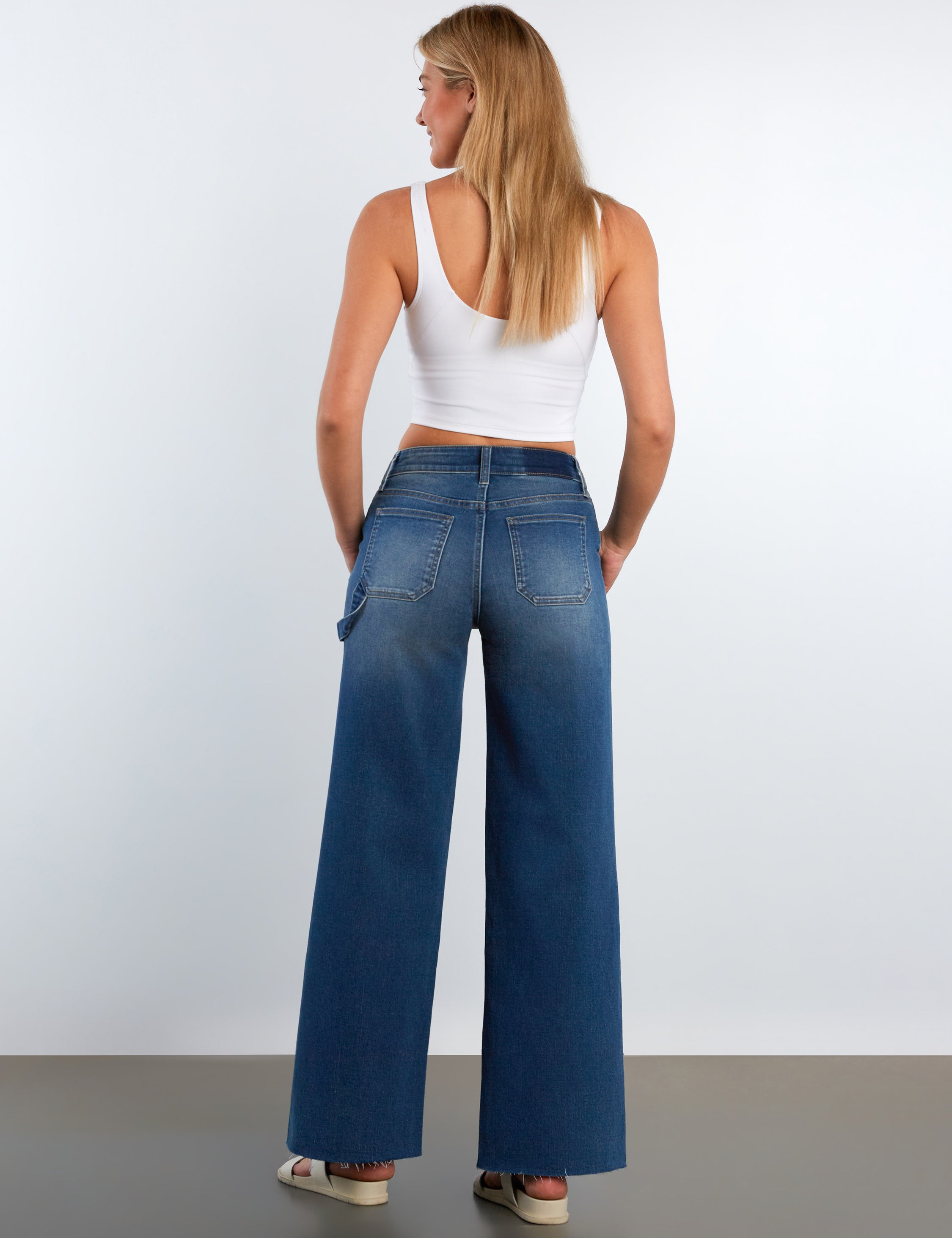 Woman wearing blue wide-leg jeans and a white top on a plain background