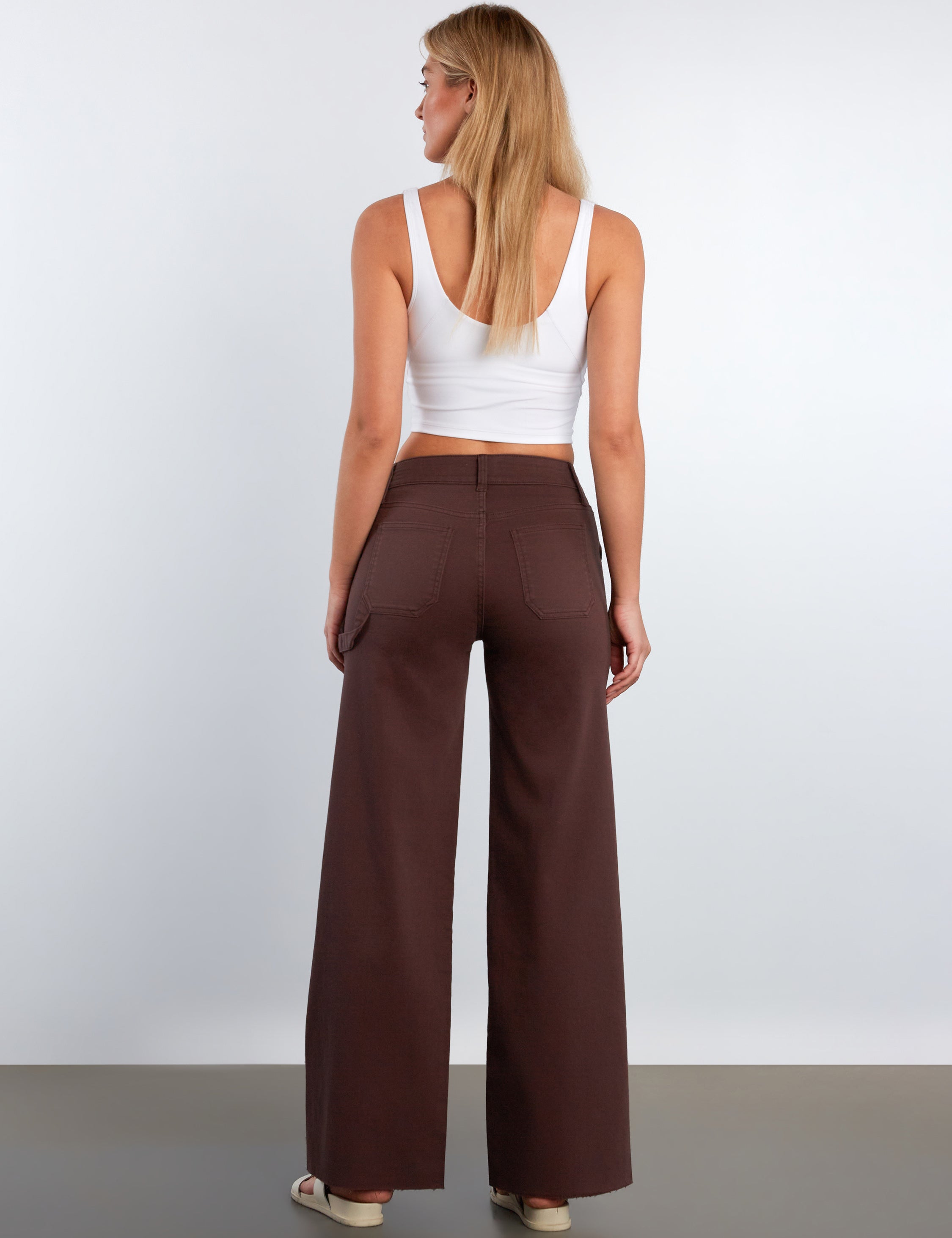 Woman wearing brown wide-leg pants and a white top on a plain background