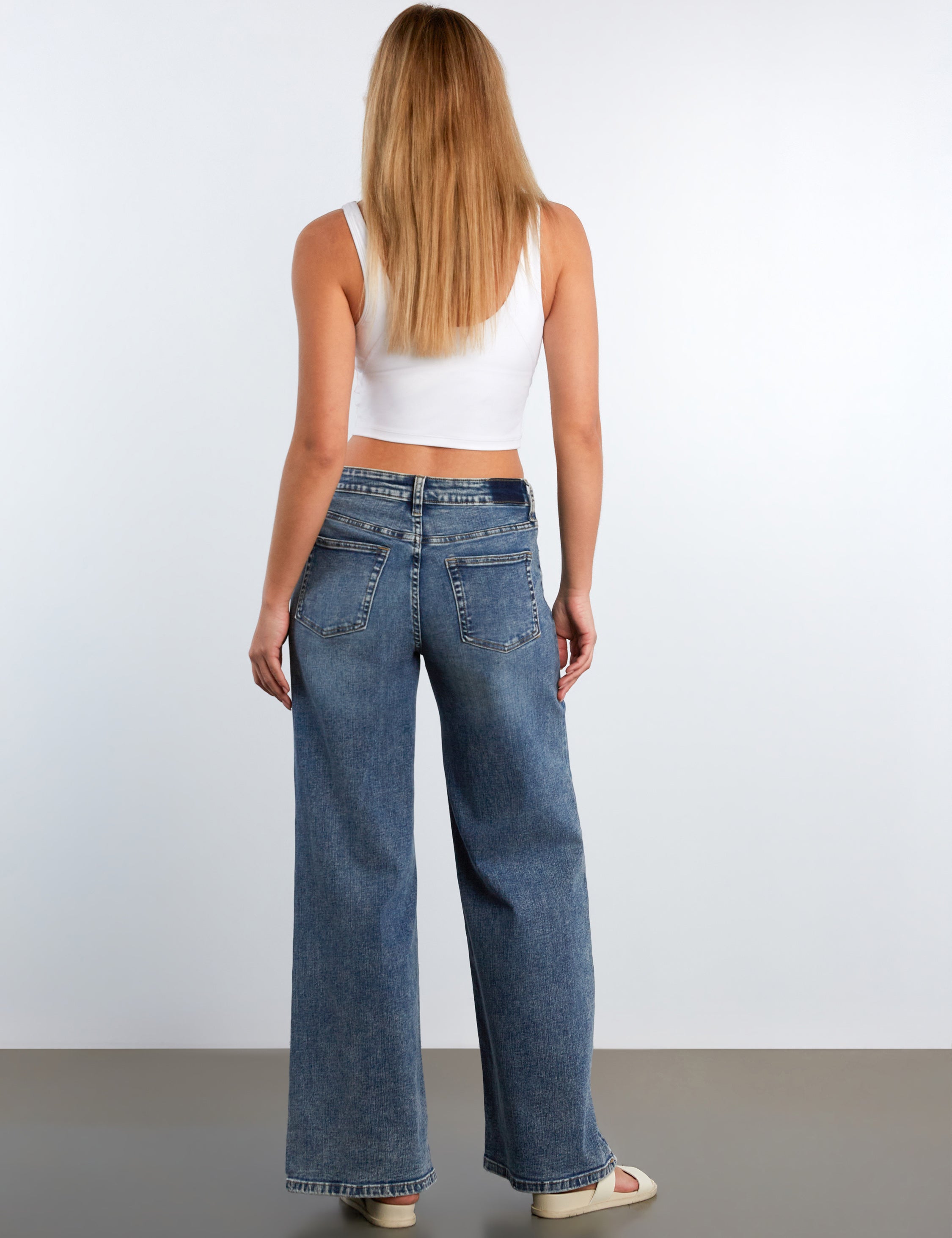 Woman wearing blue jeans and a white top on a plain background