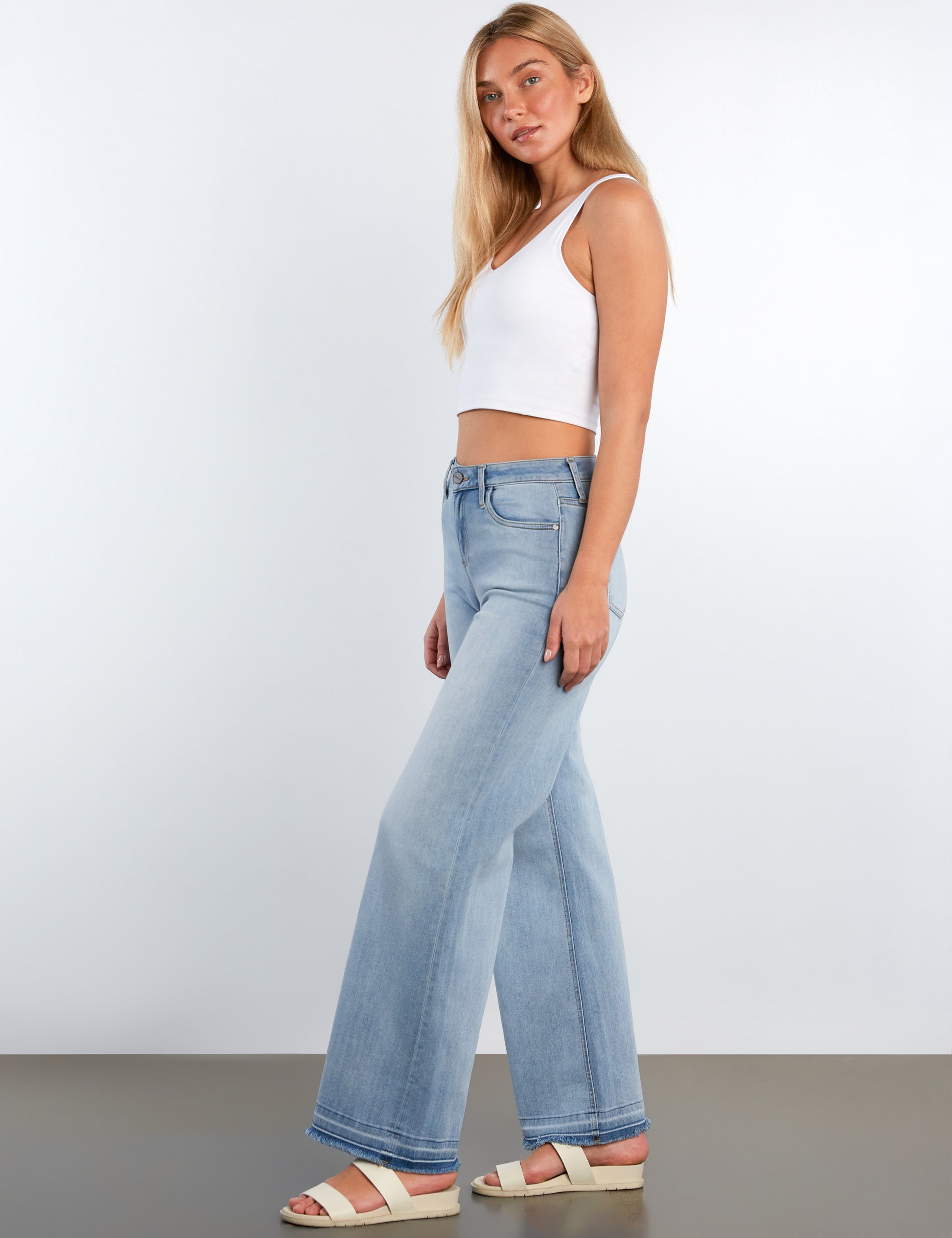 Woman wearing light blue flared jeans and a white crop top on a plain background