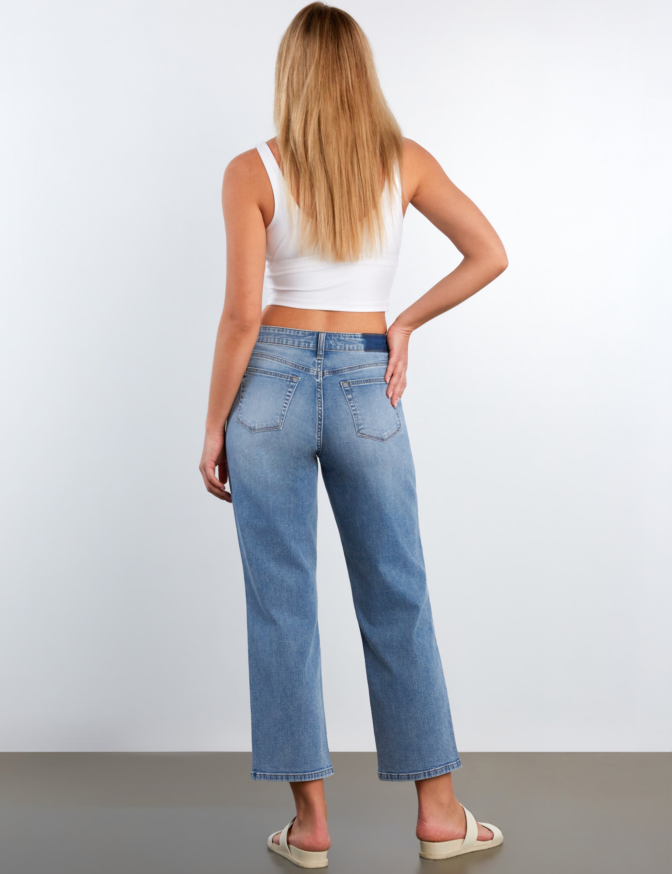 Woman wearing blue jeans and a white top on a plain background