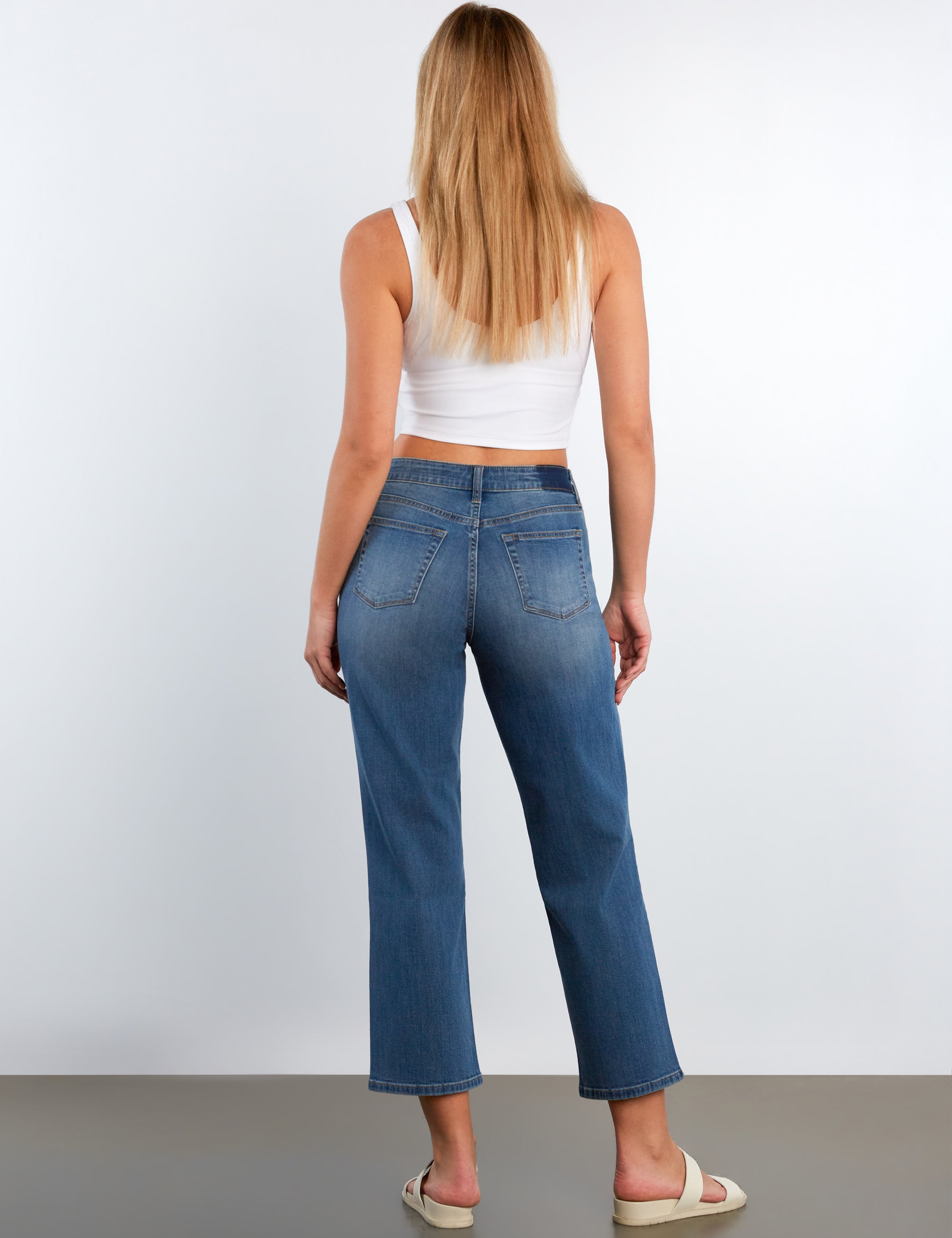 Woman wearing blue jeans and a white top on a plain background